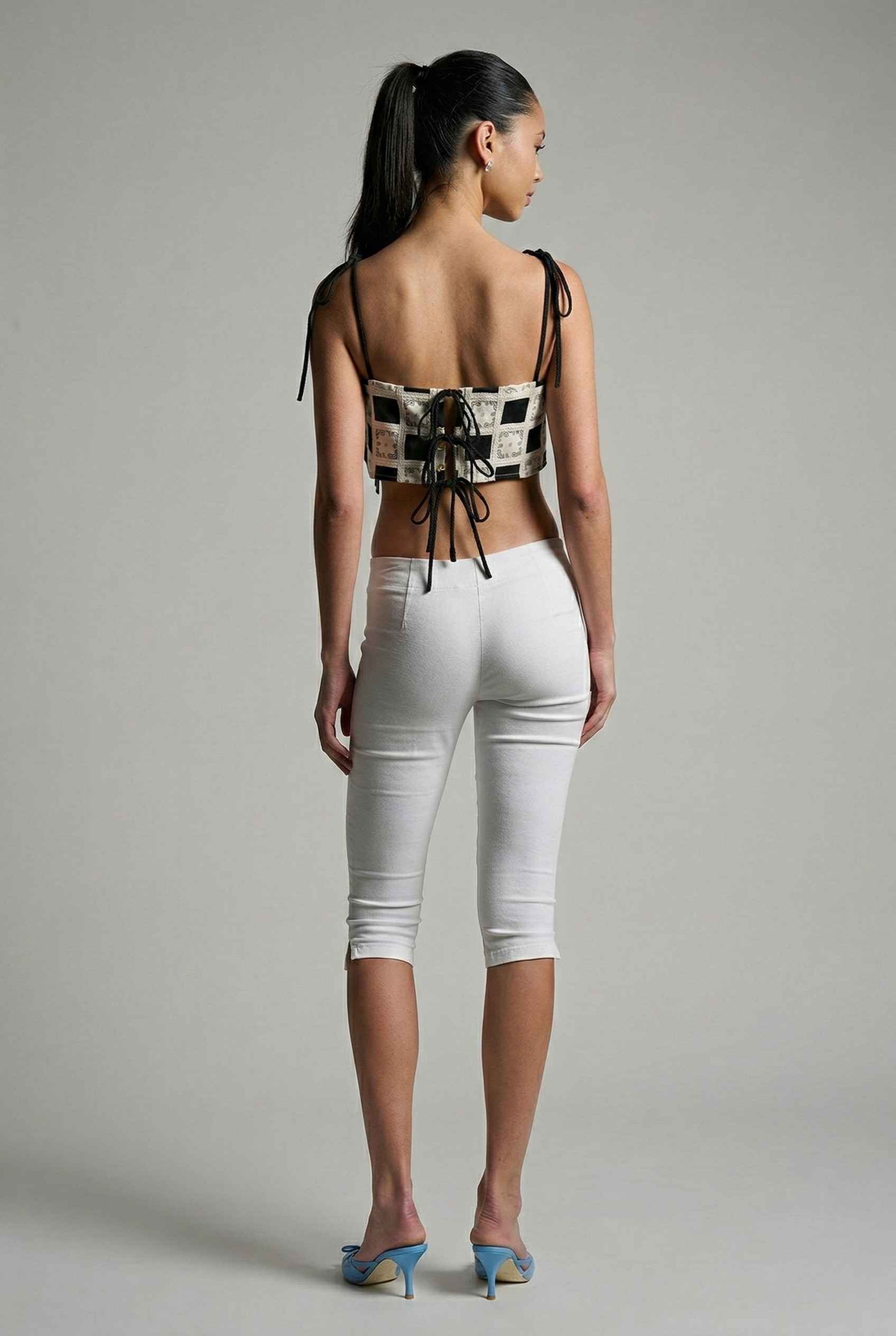 Model wearing Elodie Top in Black Jacquard Square Neck Cami with Ribbon Tie Straps with capri pants and heels on a plain background