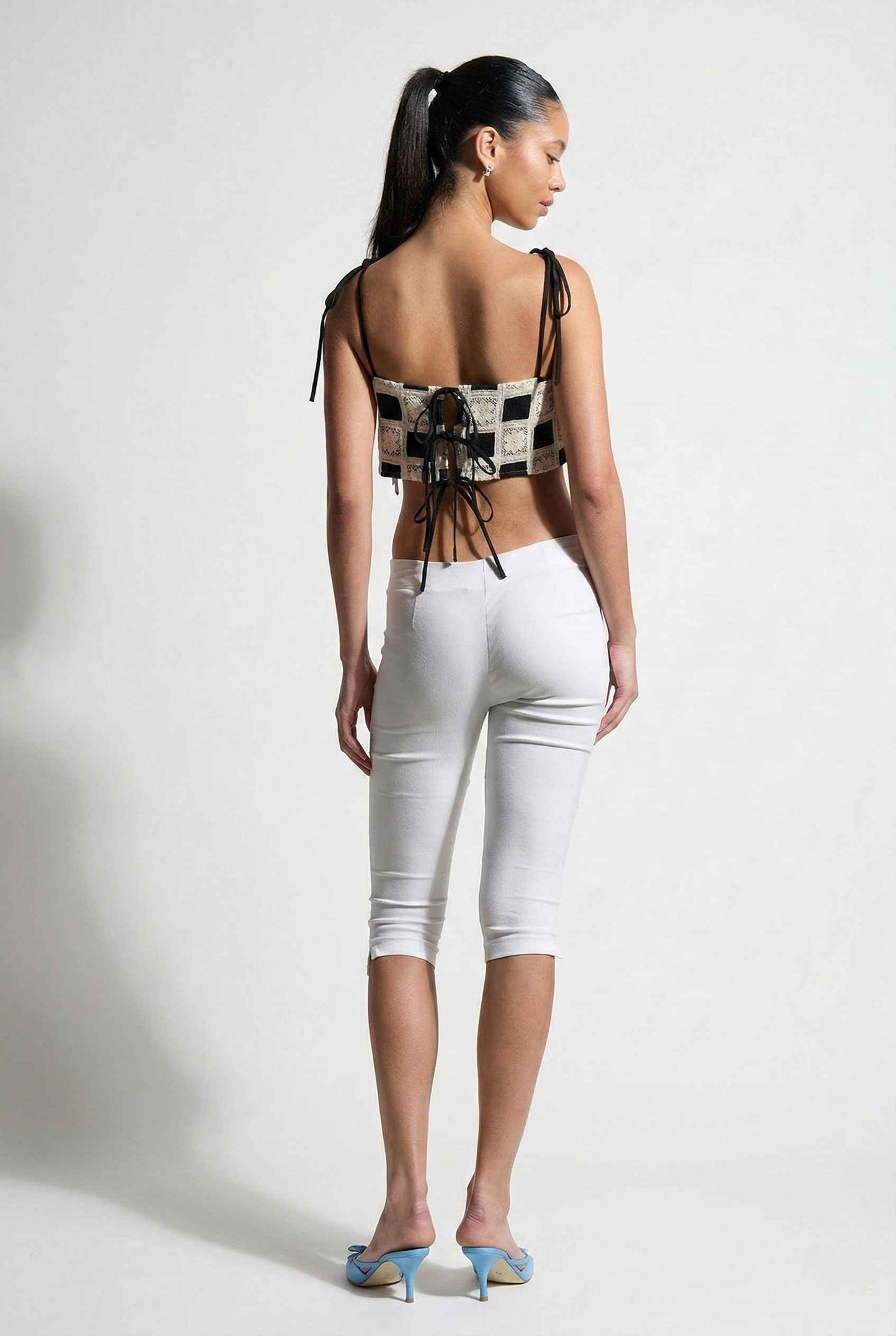 Model wearing Elodie Top in Black Jacquard Square Neck Cami with Ribbon Tie Straps with capri pants and heels on a plain background