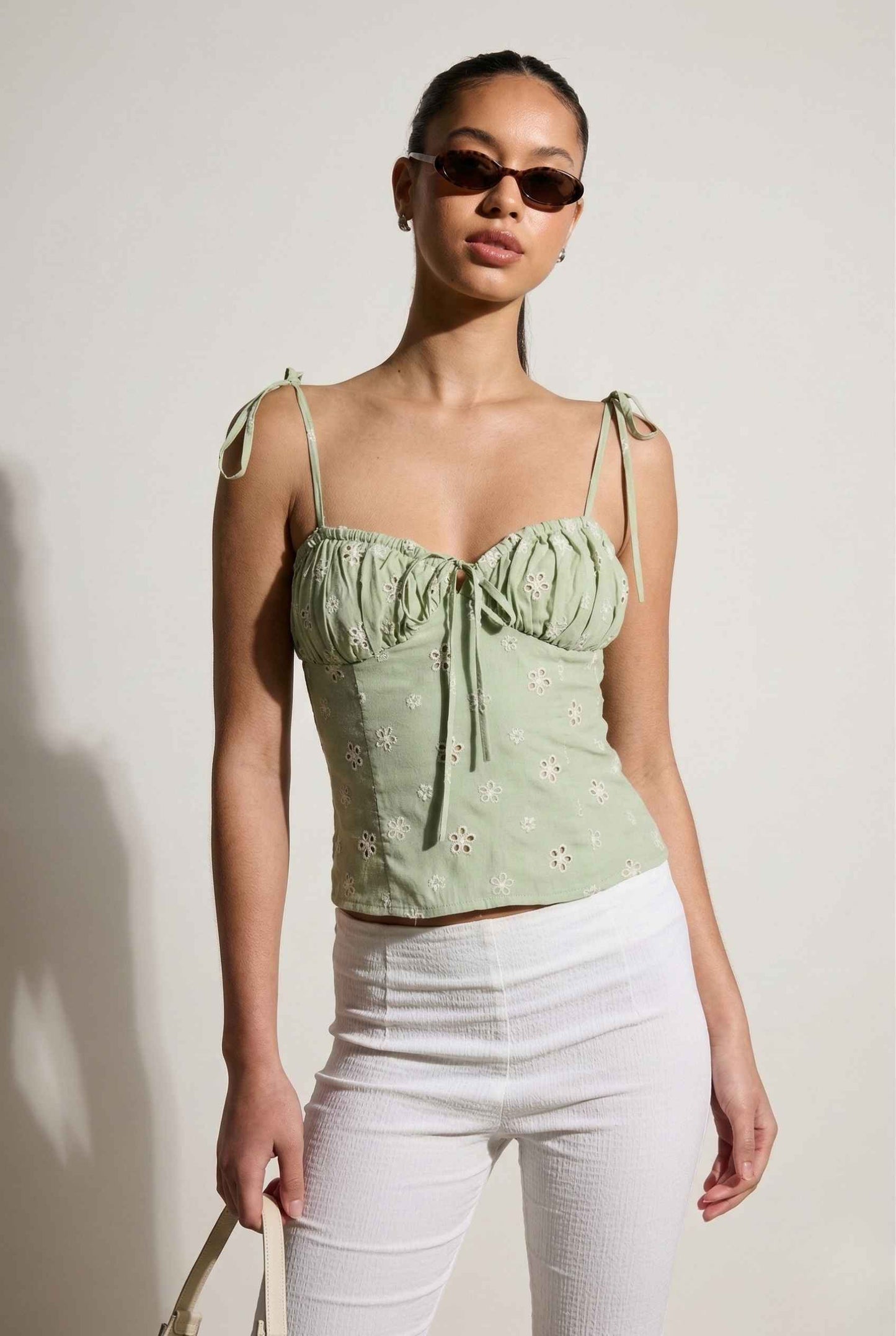 Woman wearing a Elodie Top Mint Floral Embroidered Tie-Strap Corset Top and white pants against a plain background