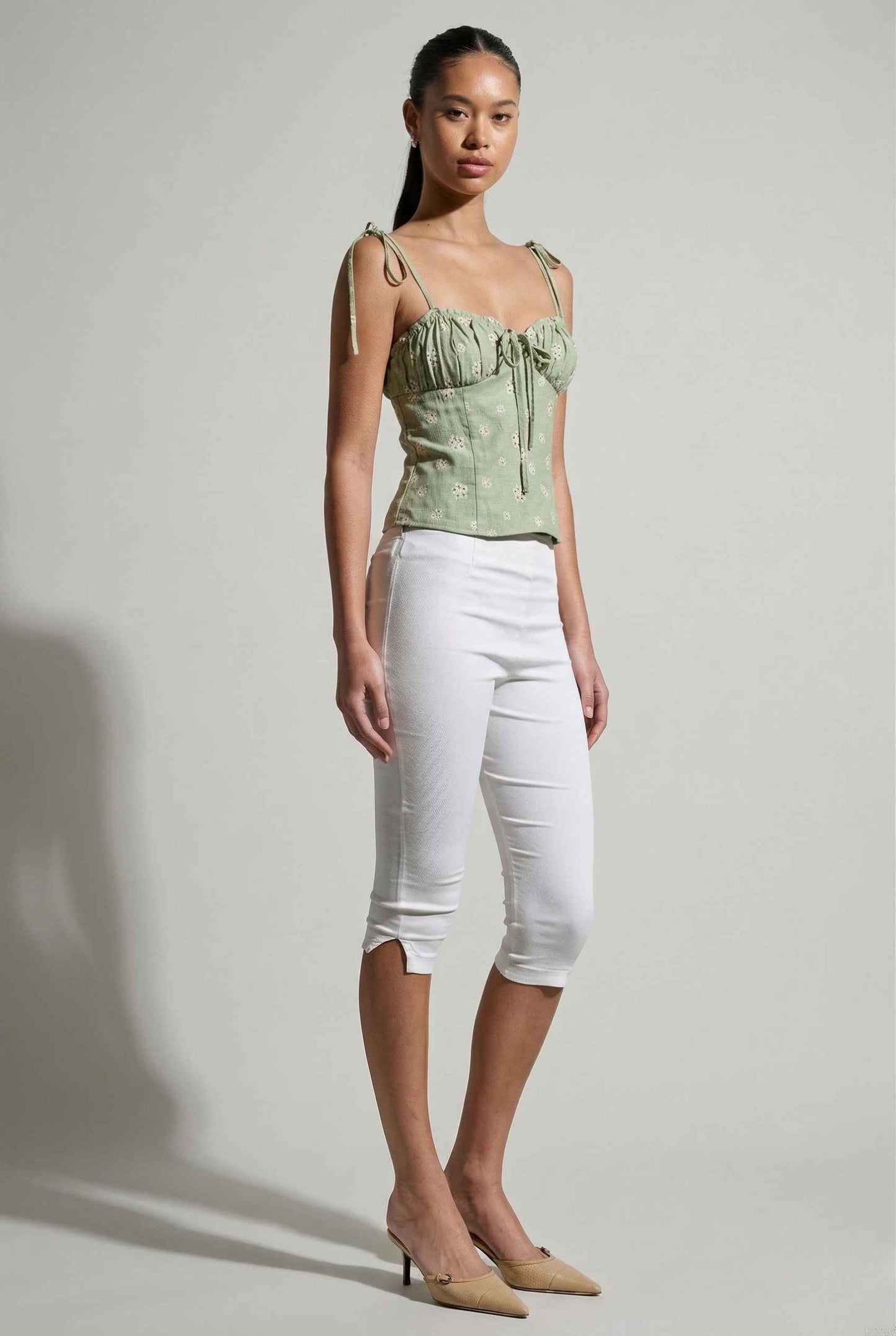 Woman wearing a Elodie Top Mint Floral Embroidered Tie-Strap Corset Top and white pants against a plain background
