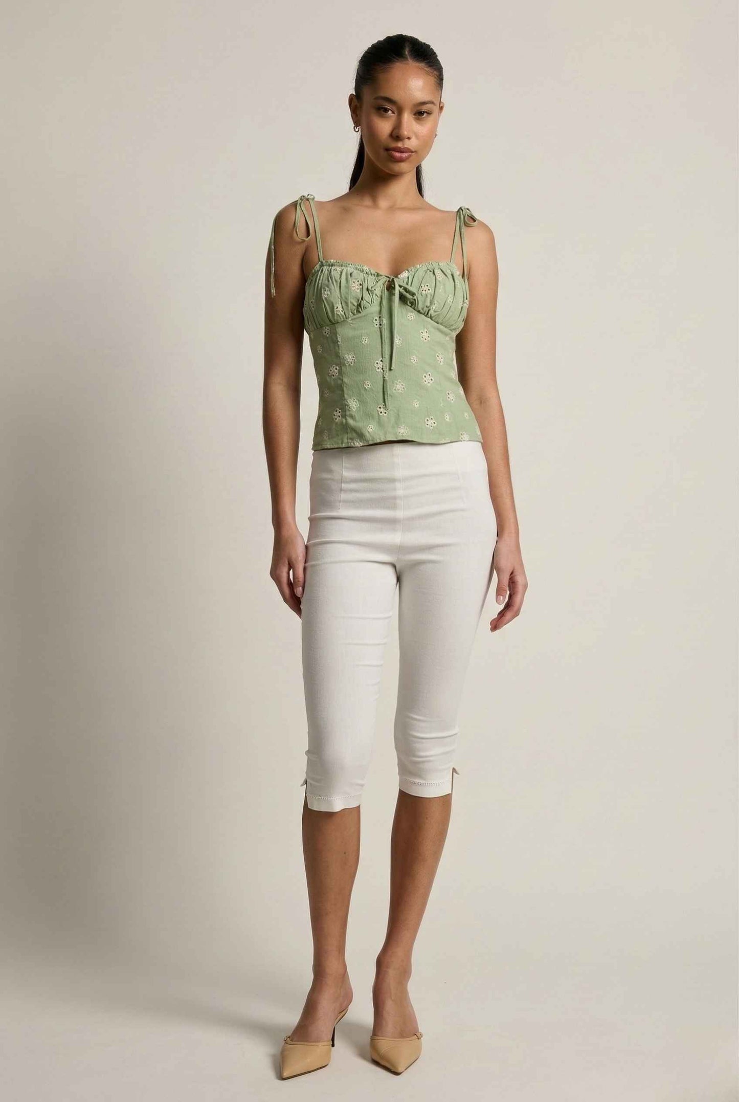 Woman wearing a Elodie Top Mint Floral Embroidered Tie-Strap Corset Top and white pants against a plain background