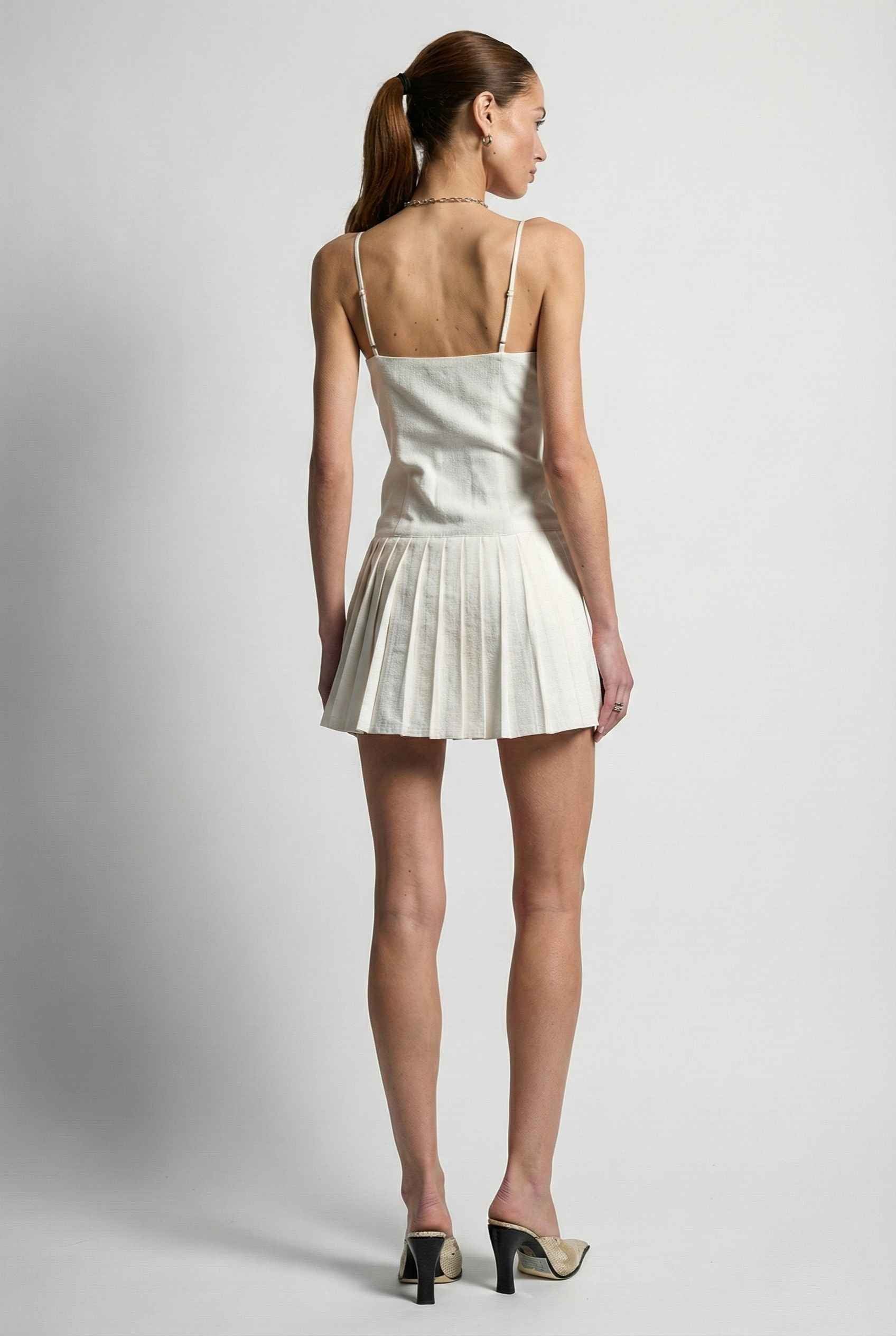 Woman wearing a Eloise Mini White Linen Blend Button Front Dress with pleated skirt on a plain background