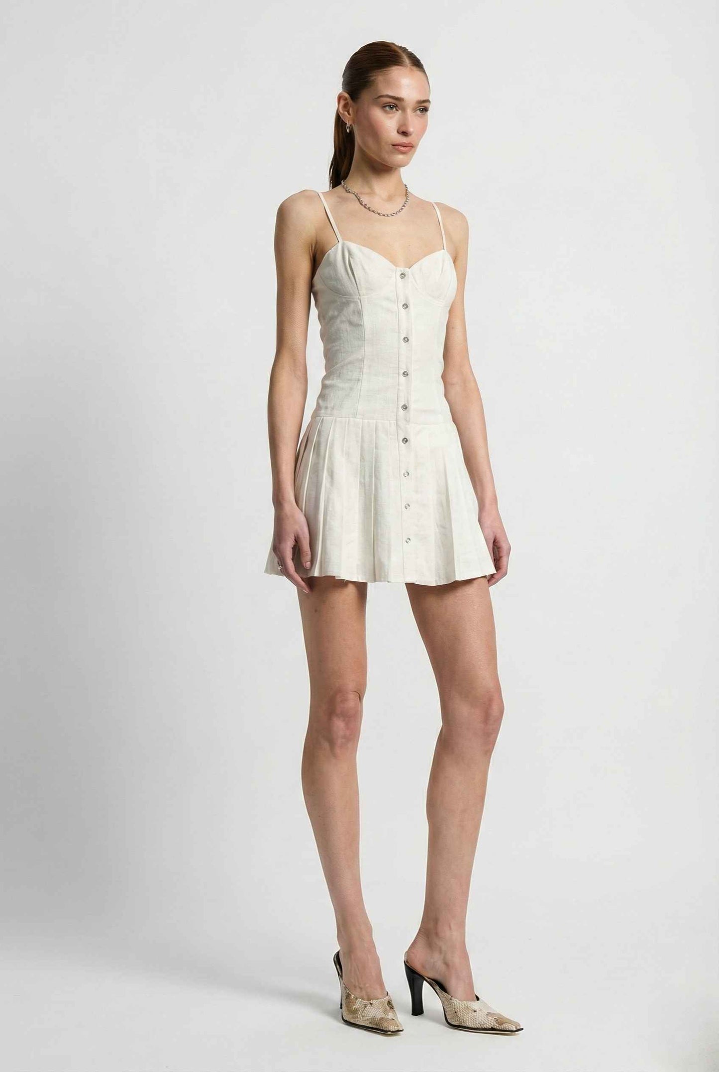 Woman wearing a Eloise Mini White Linen Blend Button Front Dress with buttons on a plain background