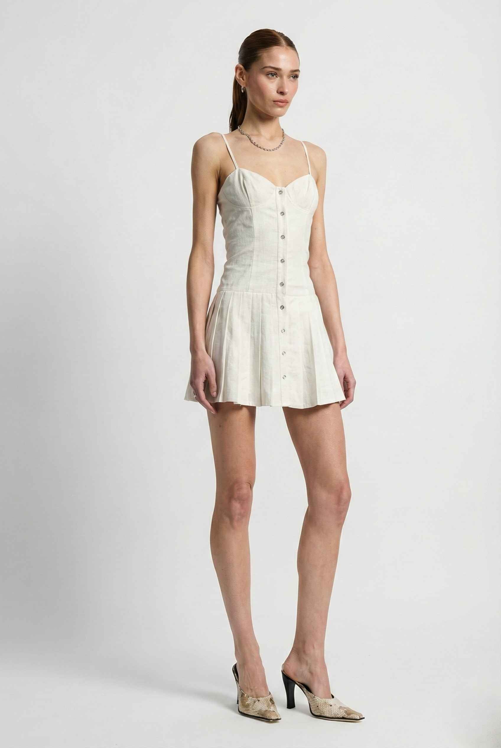 Woman wearing a Eloise Mini White Linen Blend Button Front Dress with buttons on a plain background
