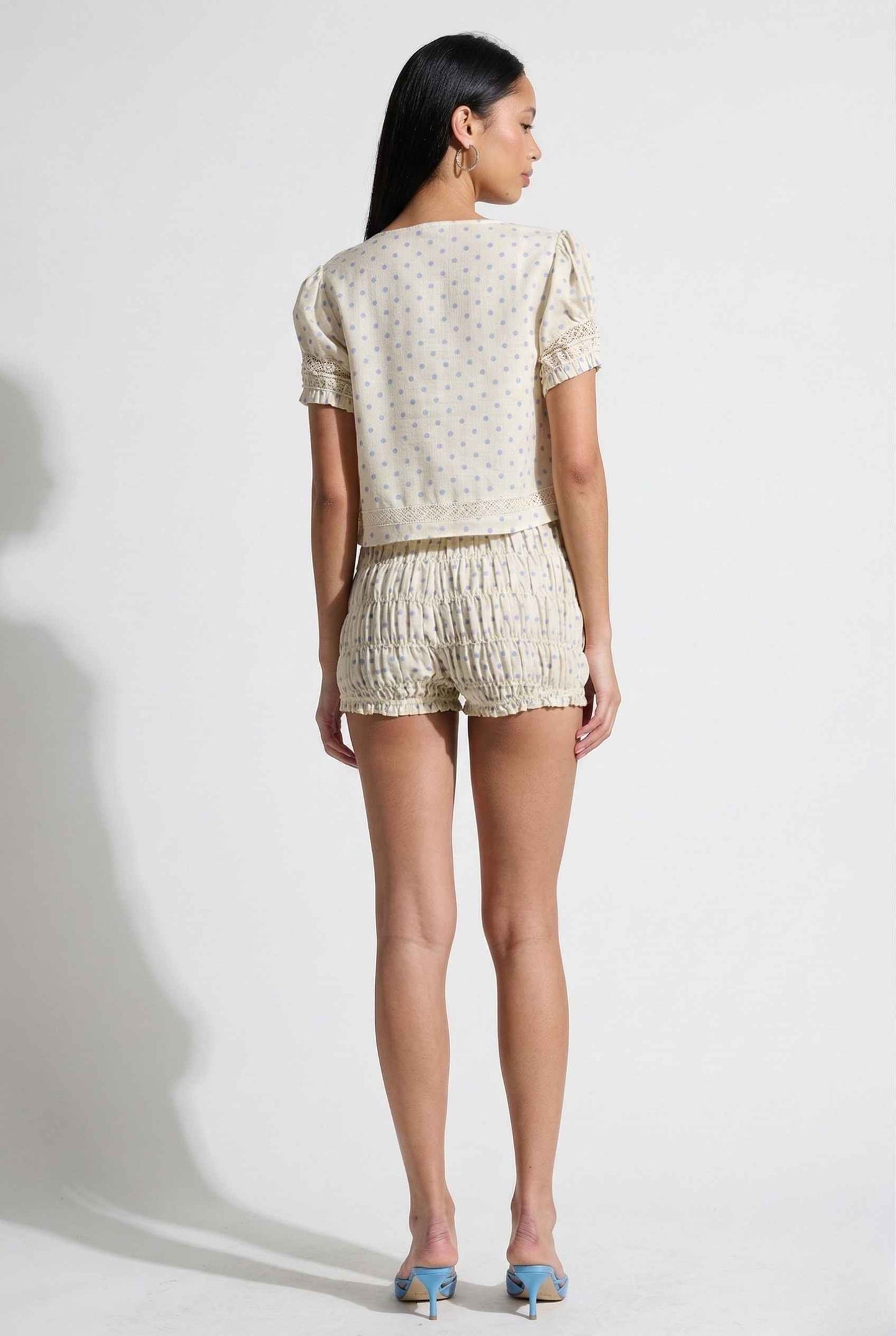 Woman wearing a Elsie Top Ivory & Blue Polka Dot Linen Tie-Front Blouse and shorts on a white background