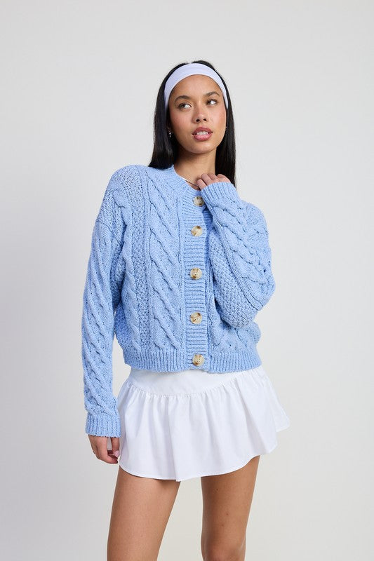 Model wearing Emory Park light blue Chunky Cable Knit Cardigan with wooden buttons over a white mini skirt