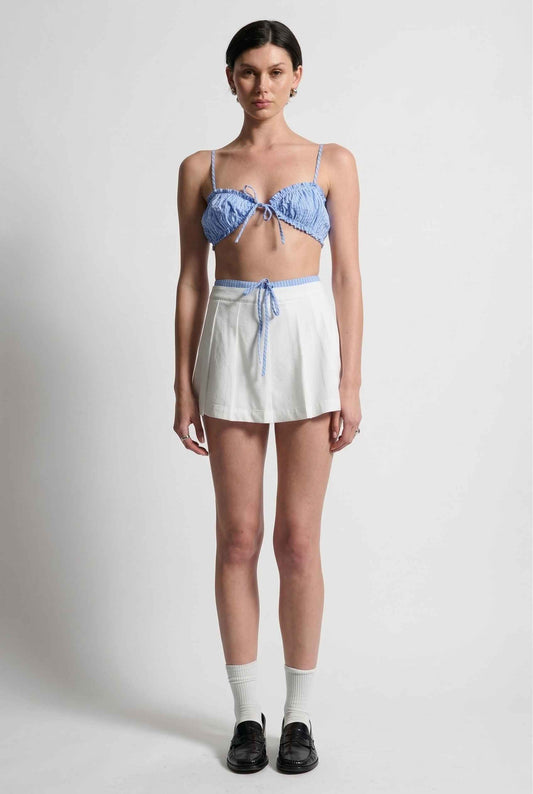 Model wearing Emory Skort in White Pleated Mini Skort with Striped Waist paired with matching bra top and shiny loafers with tall socks