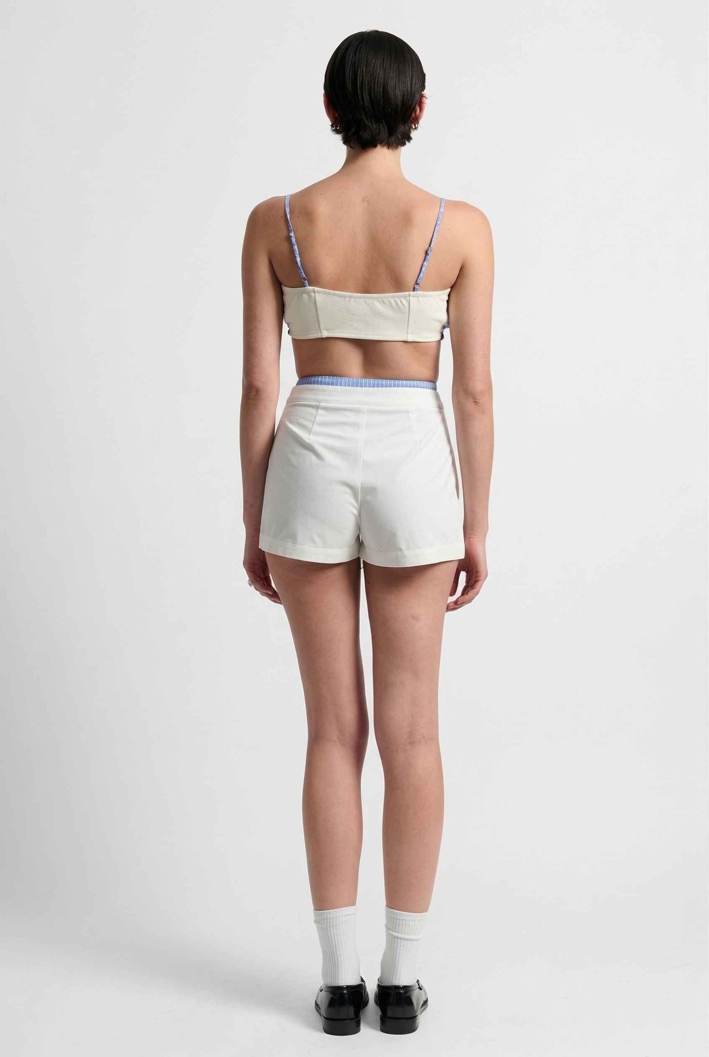 Model wearing Emory Skort in White Pleated Mini Skort with Striped Waist paired with matching bra top and shiny loafers with tall socks