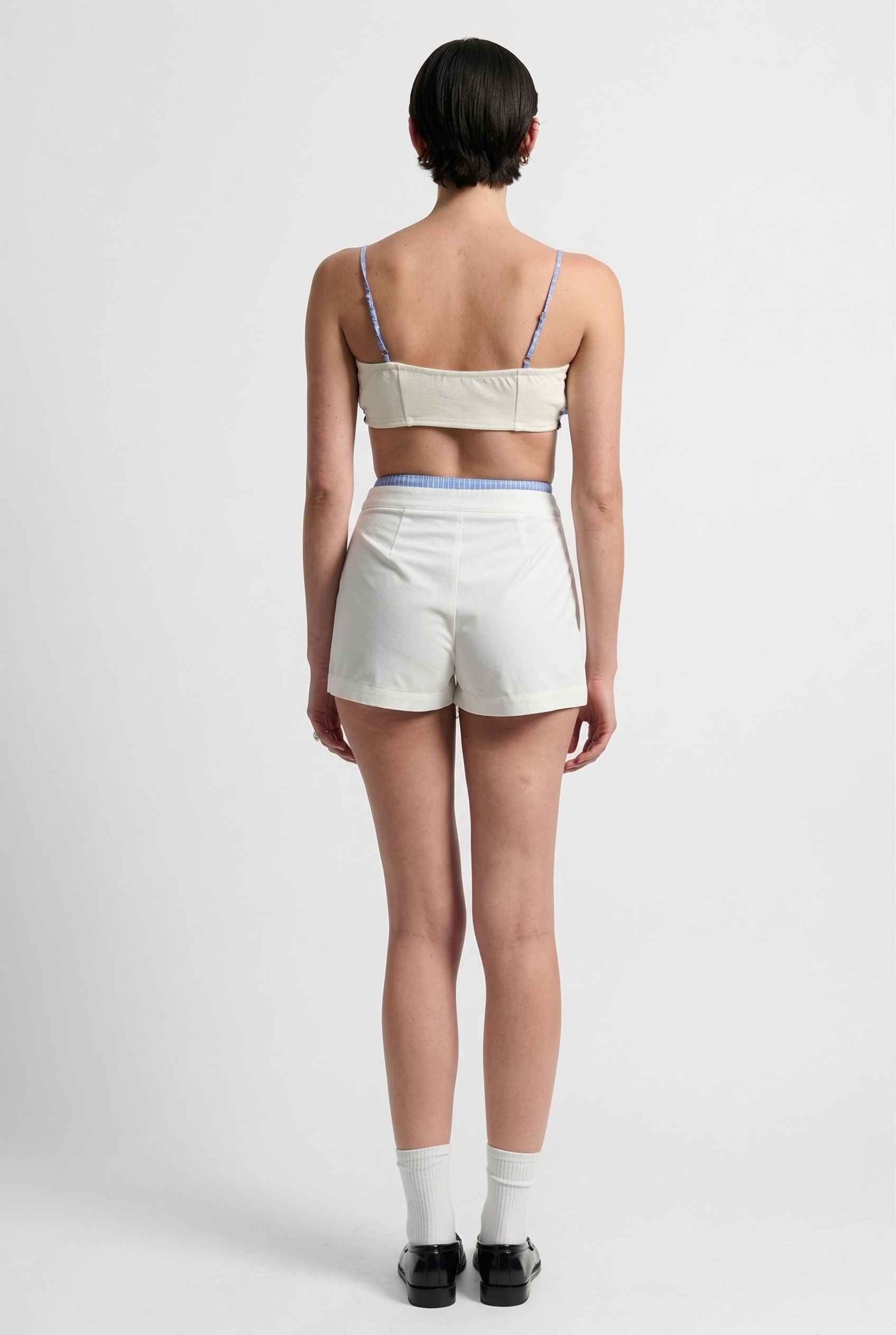 Model wearing Emory Skort in White Pleated Mini Skort with Striped Waist paired with matching bra top and shiny loafers with tall socks