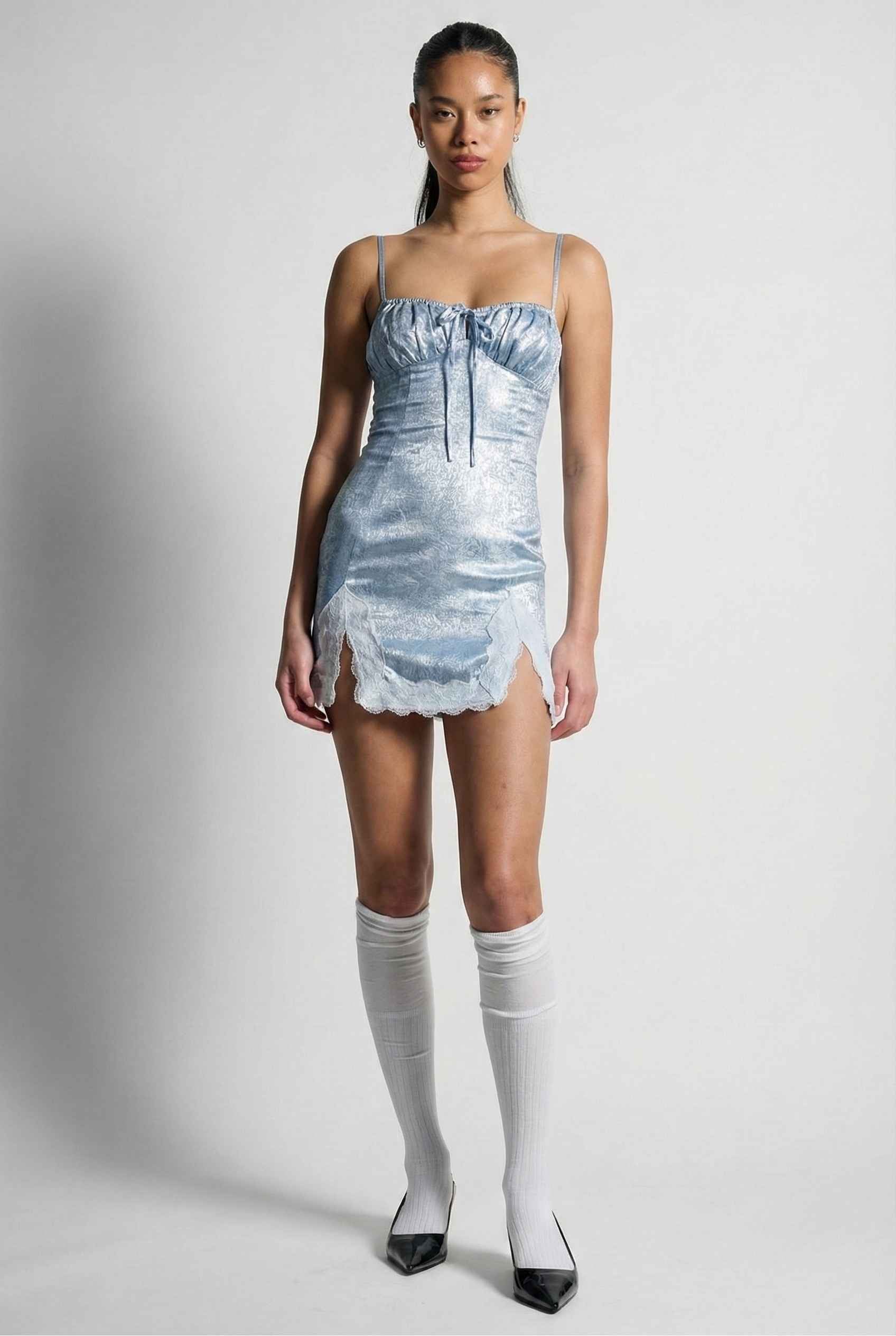 Woman wearing a Esme Mini Light Blue Satin Lace Hem Dress with white knee-high socks on a plain background