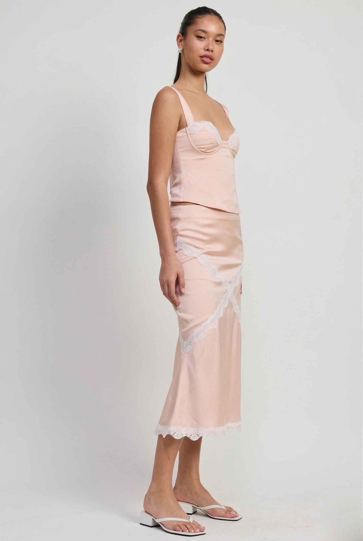 Woman wearing a Freya Skirt Blush Pink Satin Midi Skirt with White Lace Detail with lace trim on a white background