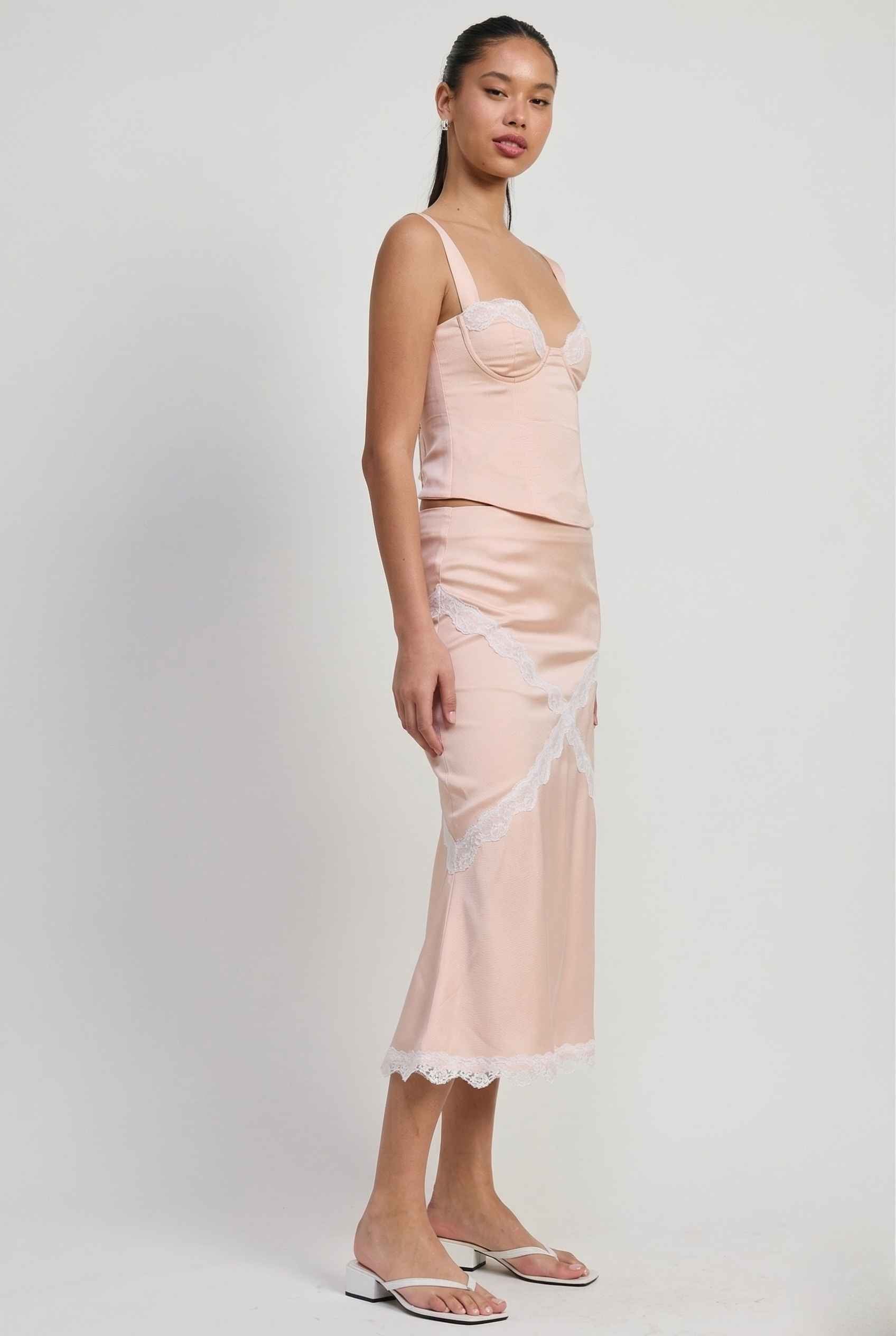 Woman wearing a Freya Skirt Blush Pink Satin Midi Skirt with White Lace Detail with lace trim on a white background