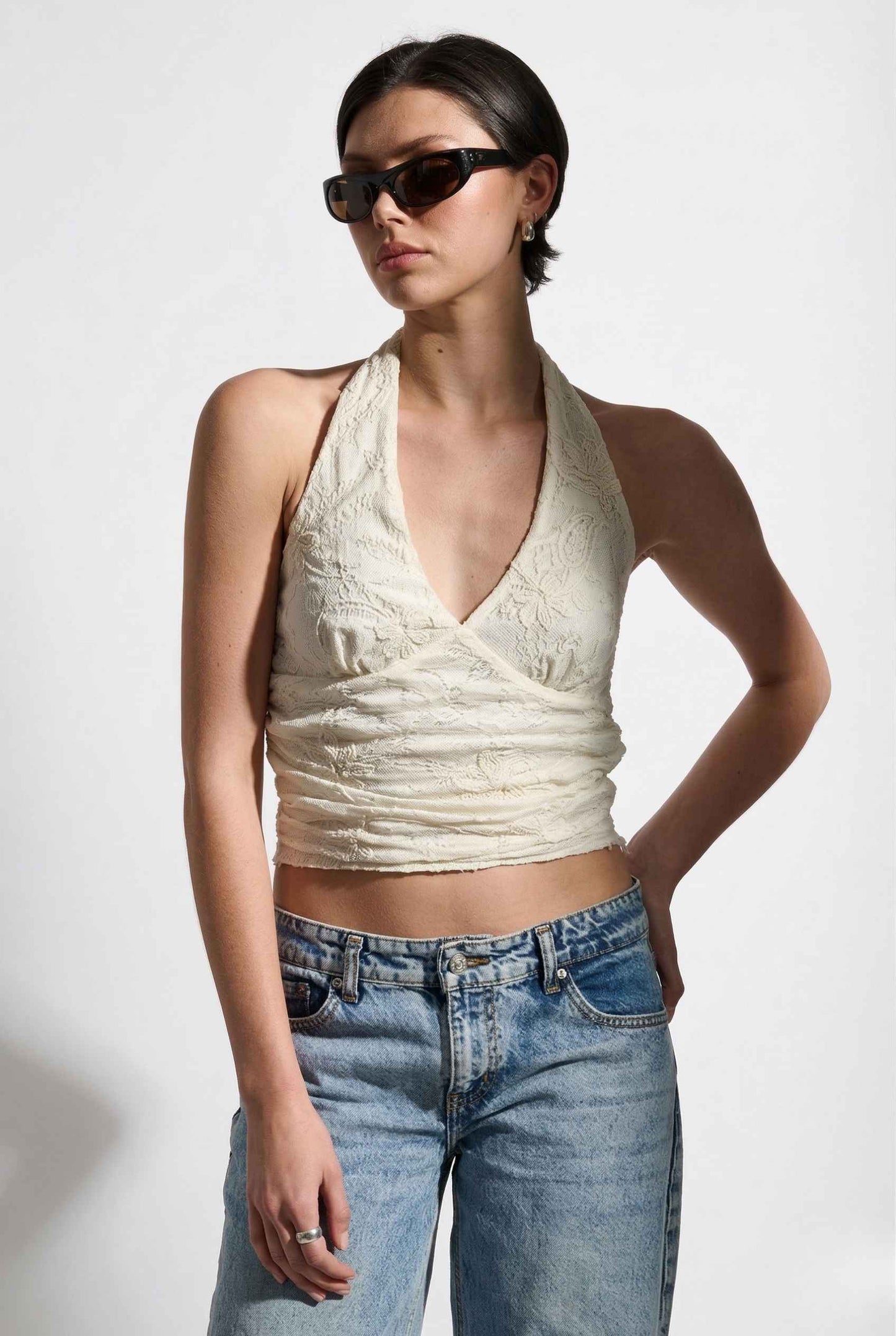 Woman wearing a Freya Top Ivory Floral Lace Wrap Halter Crop posing.