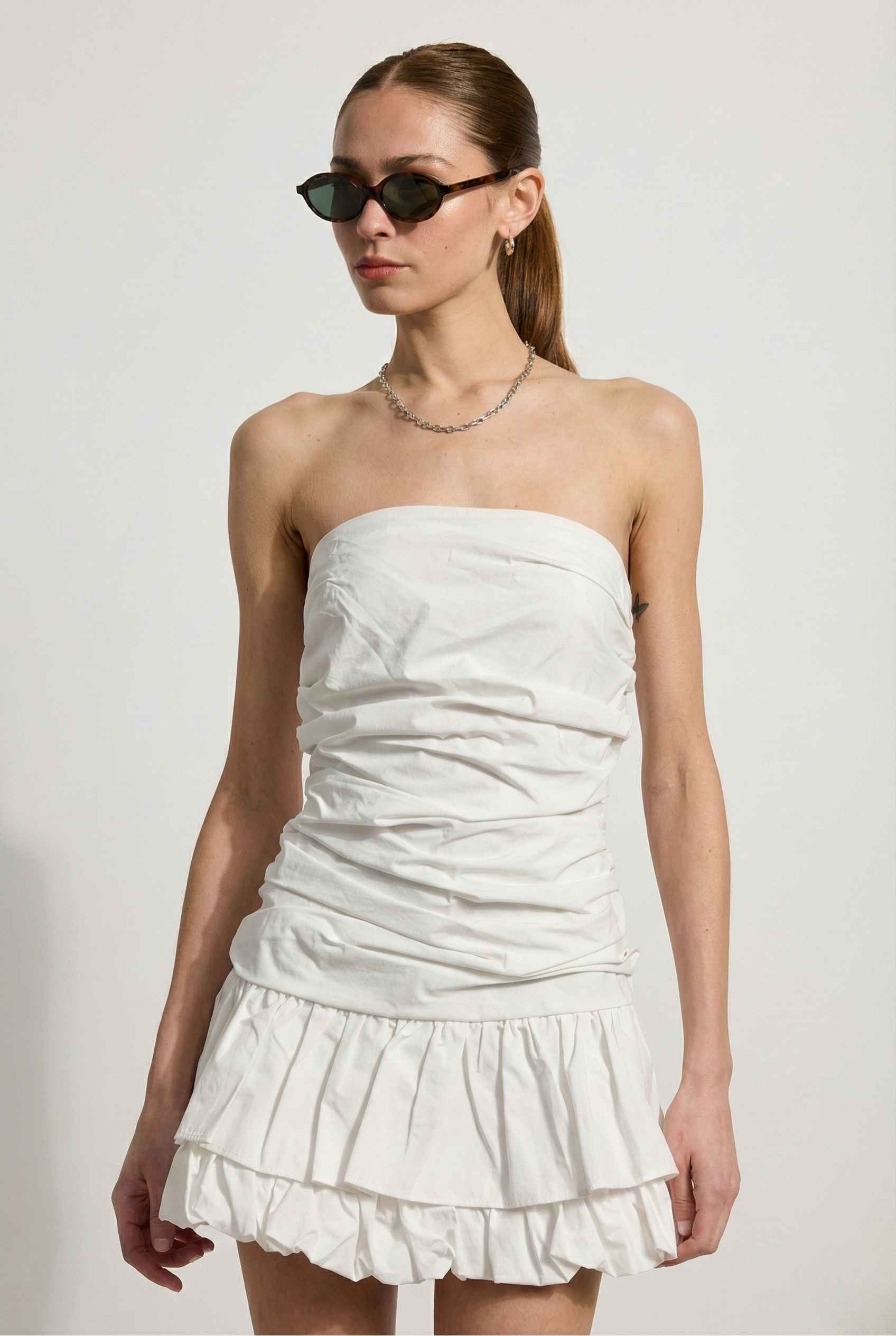 Woman wearing a Harper Mini White Ruched Strapless Cotton Dress with ruched details on a plain background