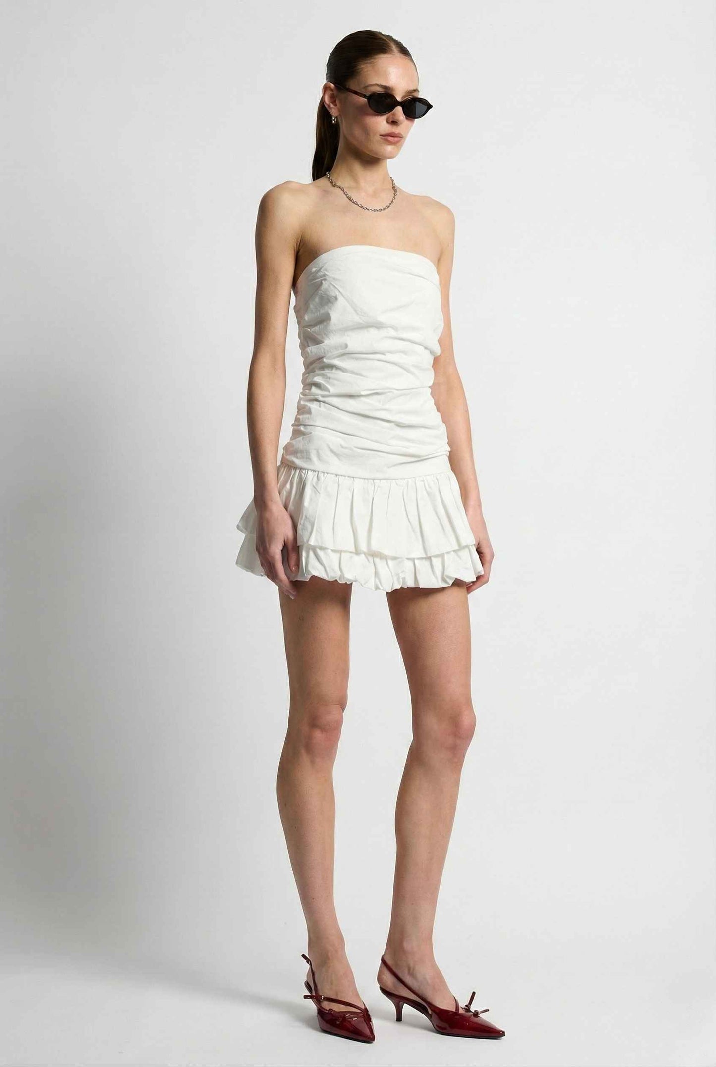 Woman wearing a Harper Mini White Ruched Strapless Cotton Dress with ruched details on a plain background