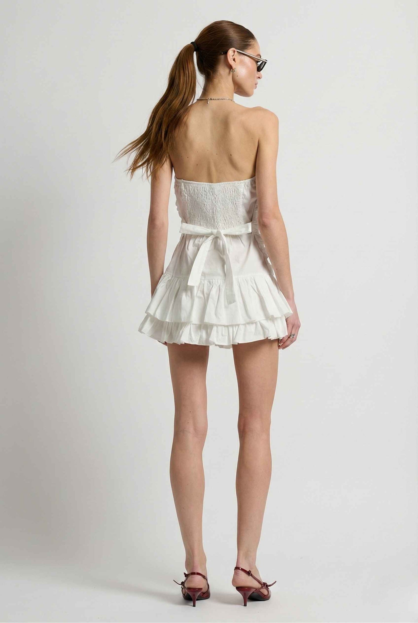Woman wearing a Harper Mini White Ruched Strapless Cotton Dress with a plain background