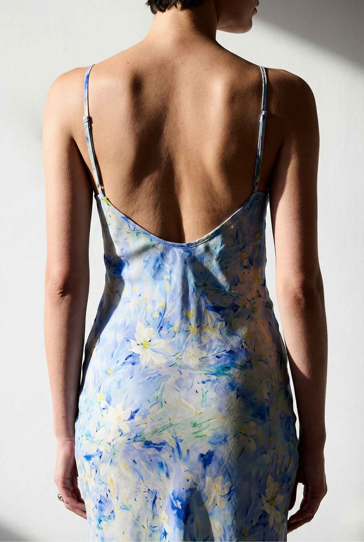 Woman wearing a Iris Midi Light Blue Floral Satin Slip Dress with an open back against a plain background