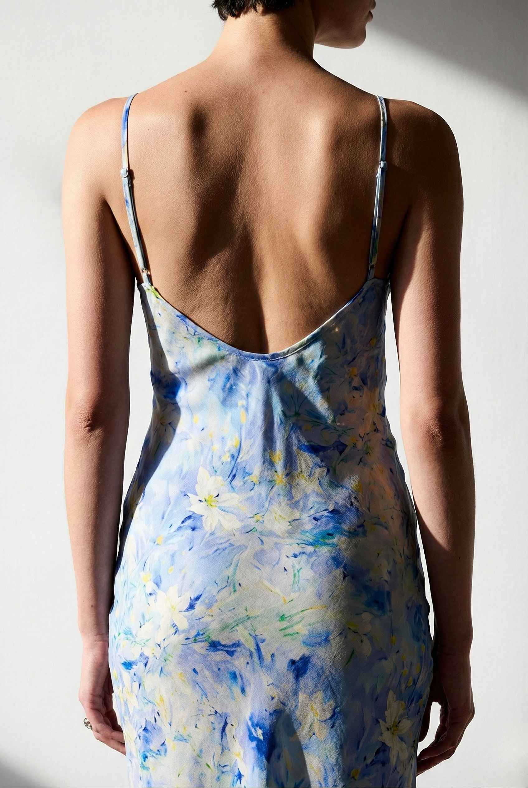 Woman wearing a Iris Midi Light Blue Floral Satin Slip Dress with an open back against a plain background
