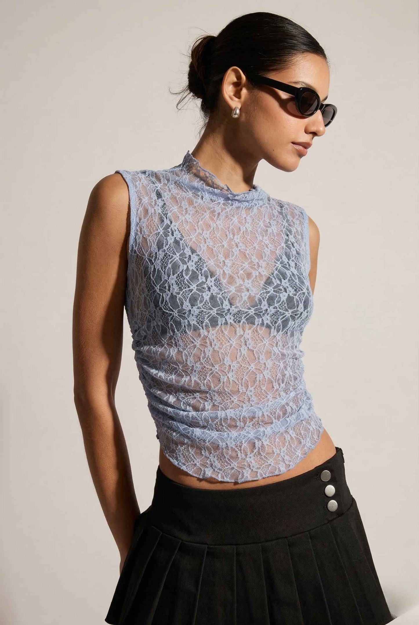 Woman wearing a Iris Top Dusty Blue Sheer Lace Sleeveless Mock Neck and black skirt against a plain background