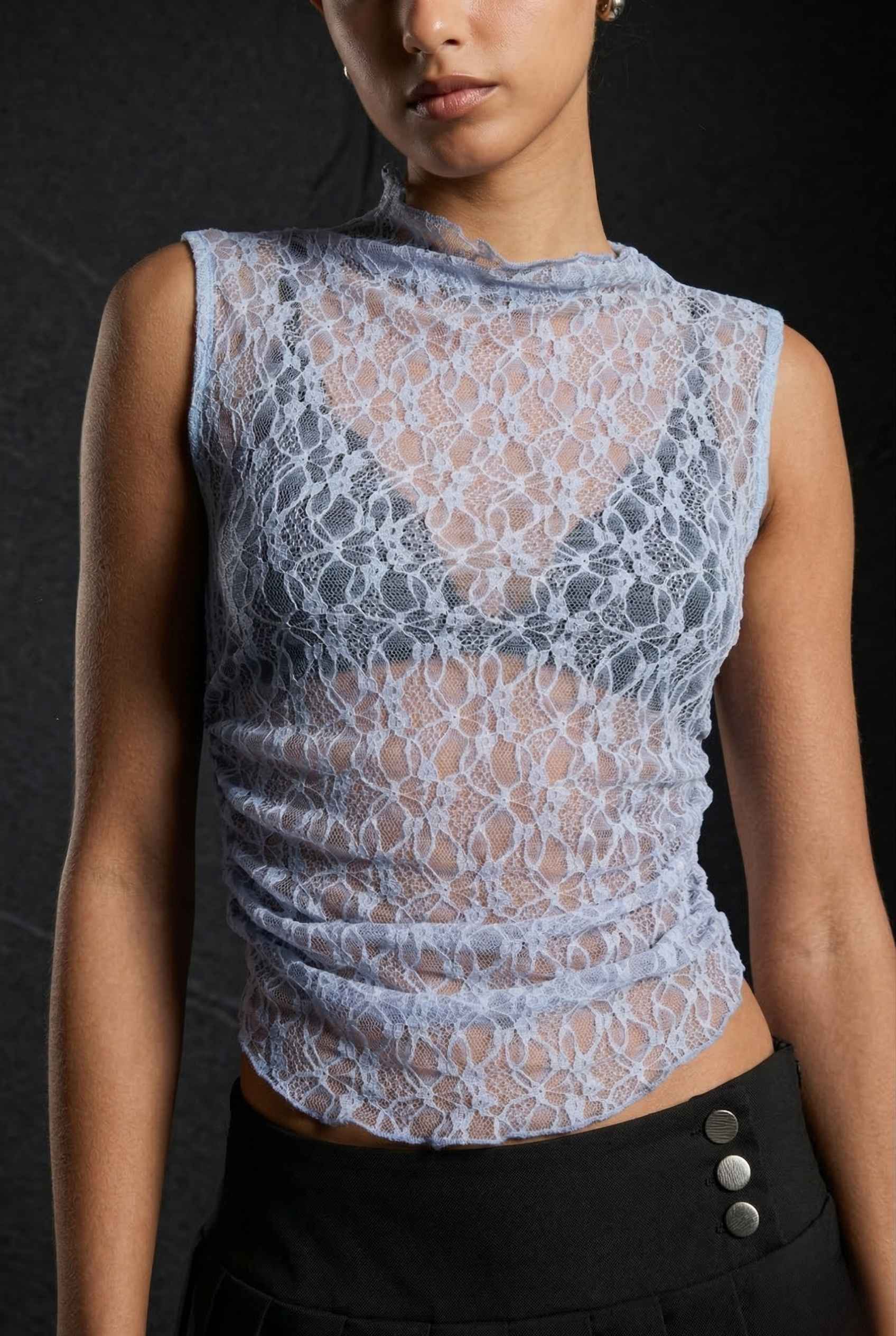 Woman wearing a Iris Top Dusty Blue Sheer Lace Sleeveless Mock Neck against a dark background