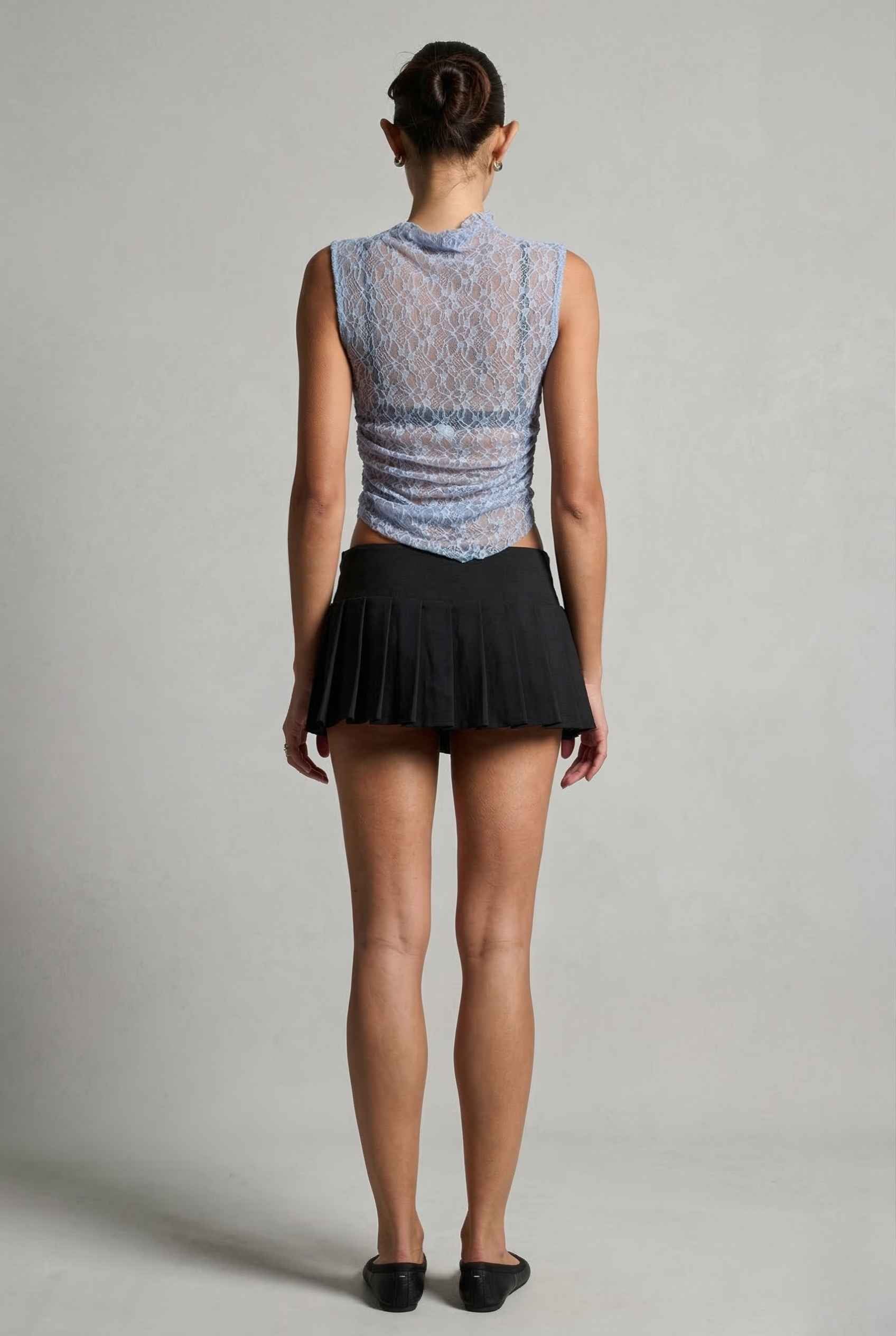 Woman wearing a Iris Top Dusty Blue Sheer Lace Sleeveless Mock Neck and black skirt on a plain background