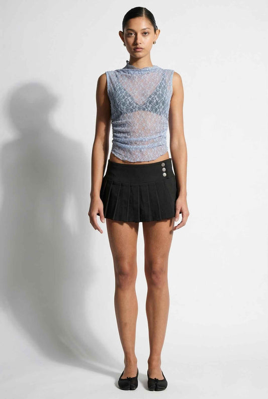 Woman wearing a Iris Top Dusty Blue Sheer Lace Sleeveless Mock Neck and black pleated skirt on a white background