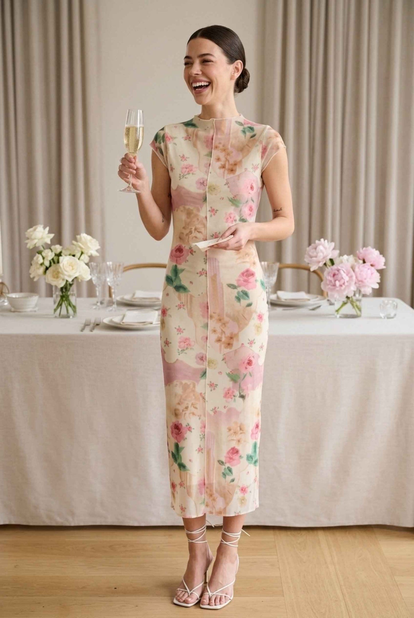 Model wearing Isabella Floral Mesh Midi Dress in Rose Floral Cap Sleeve Column Dress paired with heeled sandals laughing at wedding reception holding cocktail