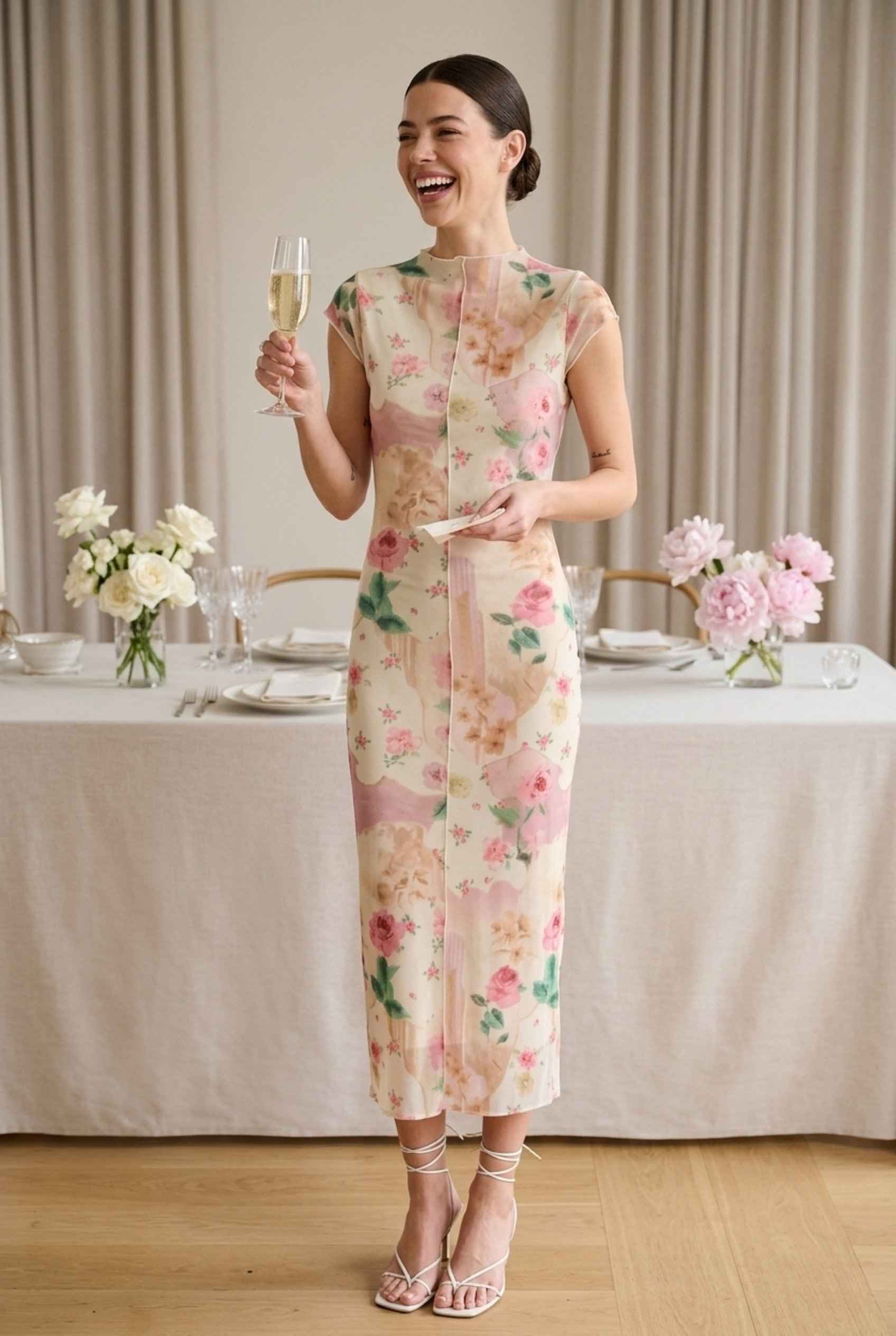Model wearing Isabella Floral Mesh Midi Dress in Rose Floral Cap Sleeve Column Dress paired with heeled sandals laughing at wedding reception holding cocktail
