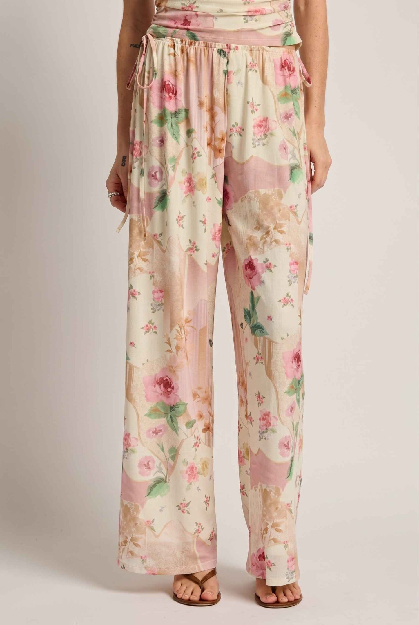 Model wearing Isabella Floral Wide-Leg Pants in Rose Floral High-Waist Trousers paired with matching high-neck tank top and heeled sandals