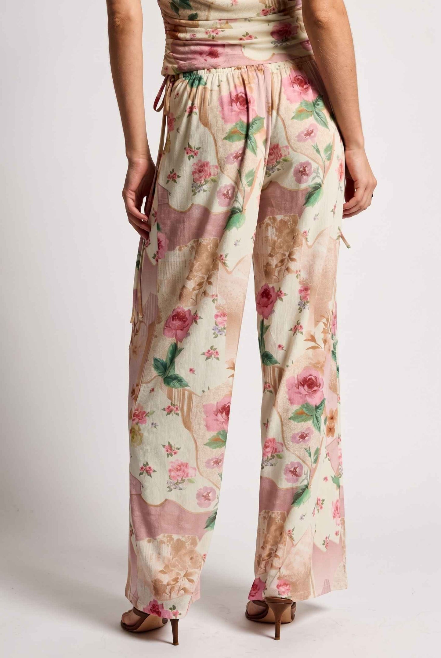 Model wearing Isabella Floral Wide-Leg Pants in Rose Floral High-Waist Trousers paired with matching high-neck tank top and heeled sandals back view