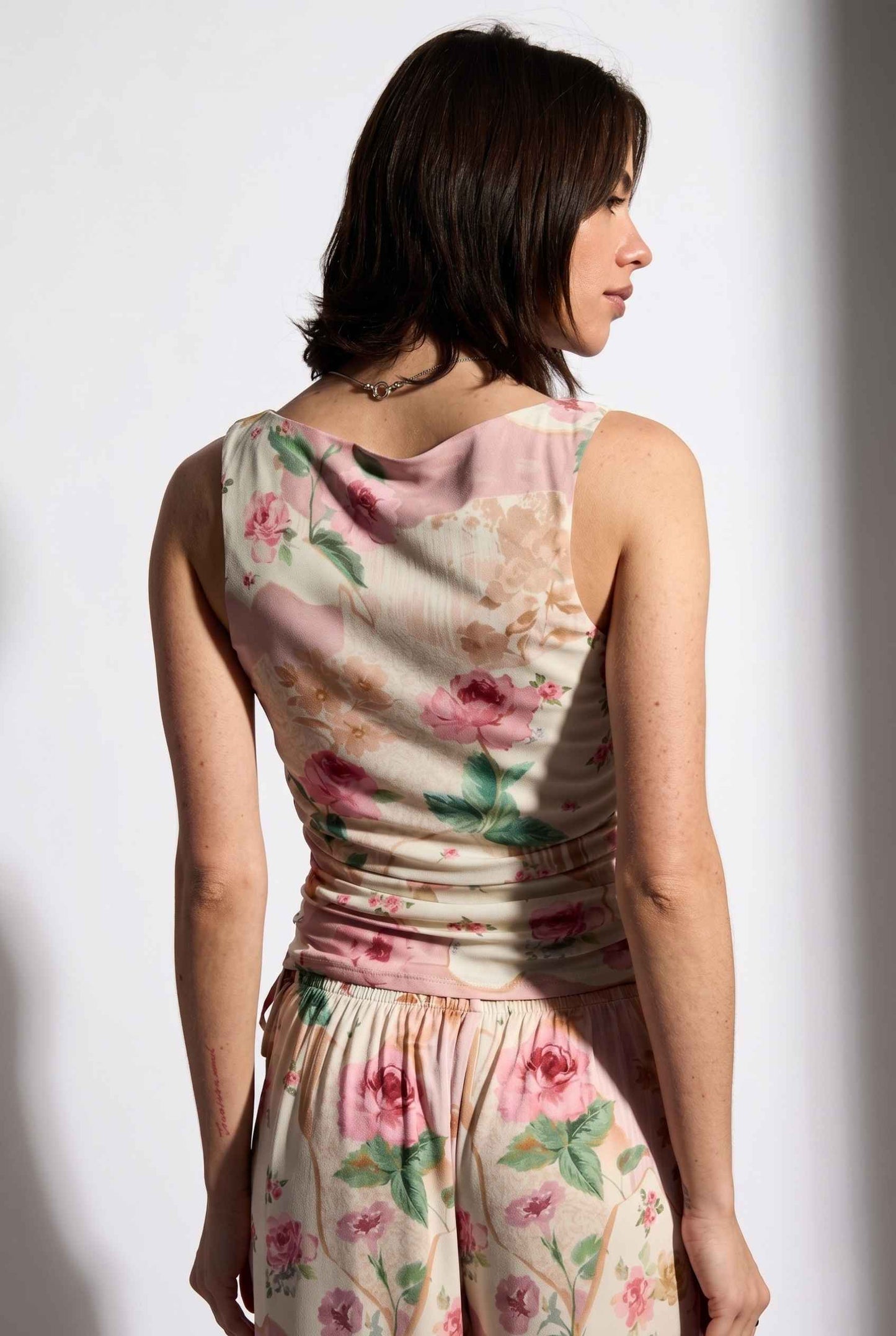 Model wearing Isabella Ruched Floral Tank in Rose Floral Sleeveless Mesh Top paired with matching bottoms close up back view