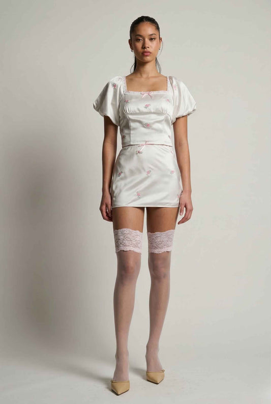 Woman wearing a Isadora Top Ivory Floral Satin Square Neck Blouse with lace details on a plain background