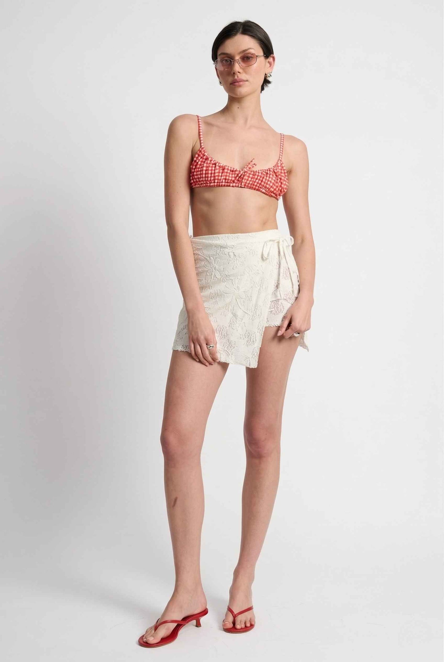 Model wearing Isla Skirt in Ivory Floral Lace Mini Wrap Skirt & Swim Cover-Up with gingham bikini top and matching sandals