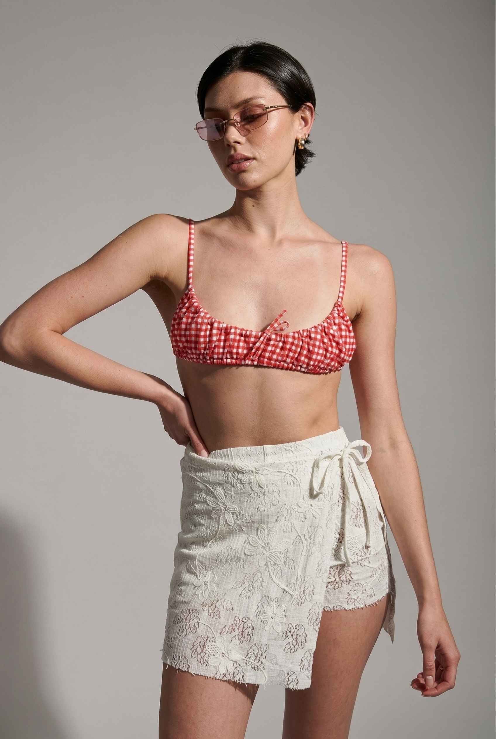 Model wearing Isla Skirt in Ivory Floral Lace Mini Wrap Skirt & Swim Cover-Up with gingham bikini top and sunglasses