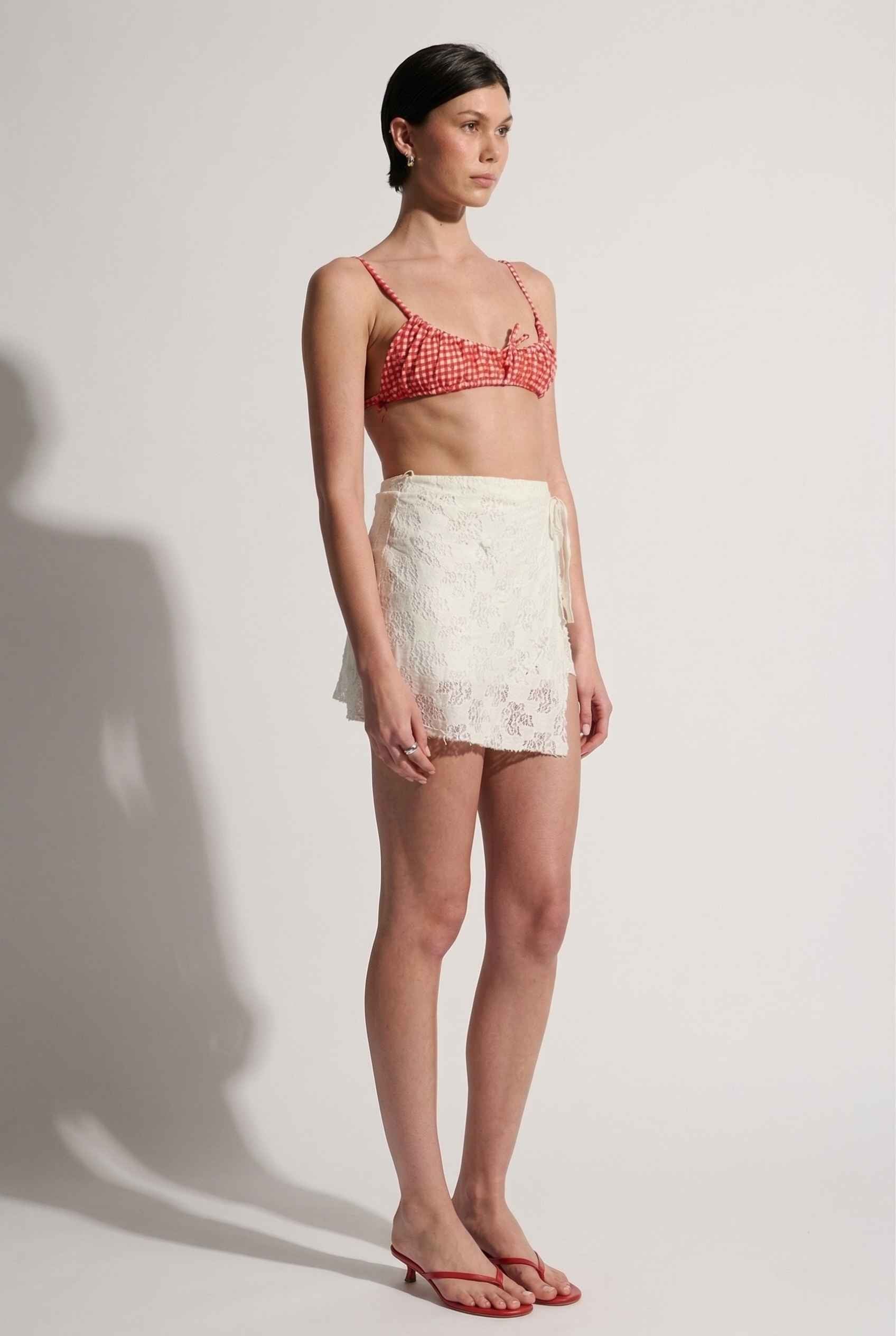 Model wearing Isla Skirt in Ivory Floral Lace Mini Wrap Skirt & Swim Cover-Up with gingham bikini top and matching sandals