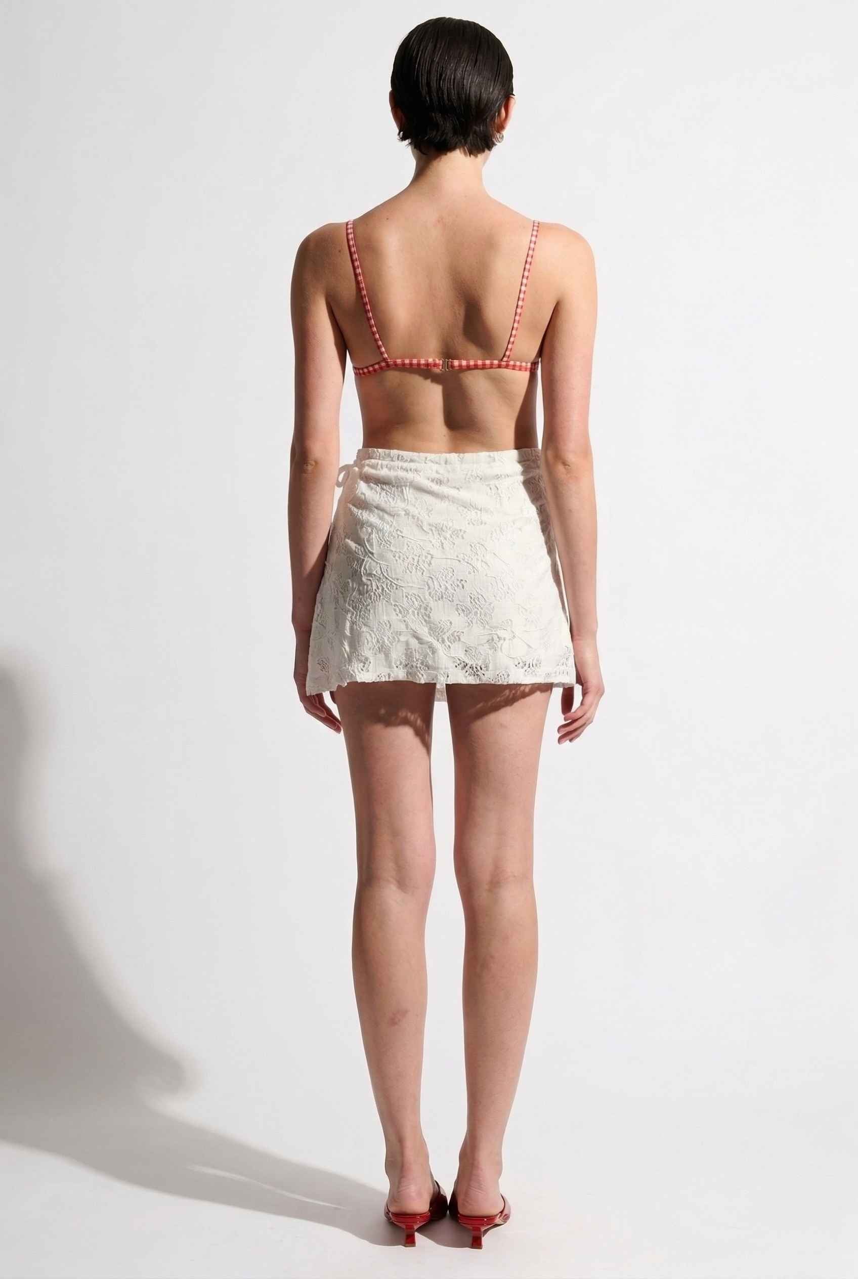 Model wearing Isla Skirt in Ivory Floral Lace Mini Wrap Skirt & Swim Cover-Up with gingham bikini top and matching sandals