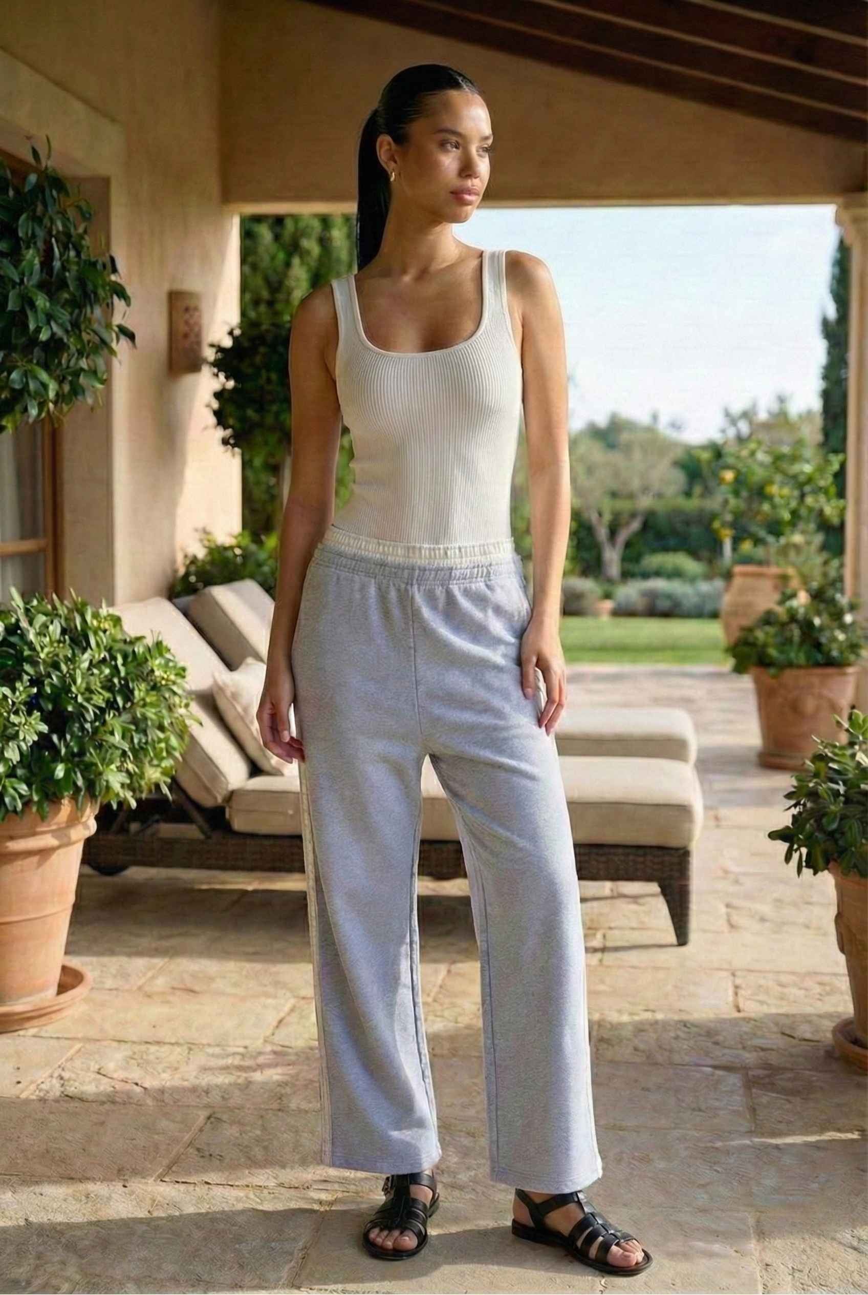 Model wearing Jamie Pants in Blue Double-Waist Boxer Style Trousers with basic tank top and sandals standing on luxury patio