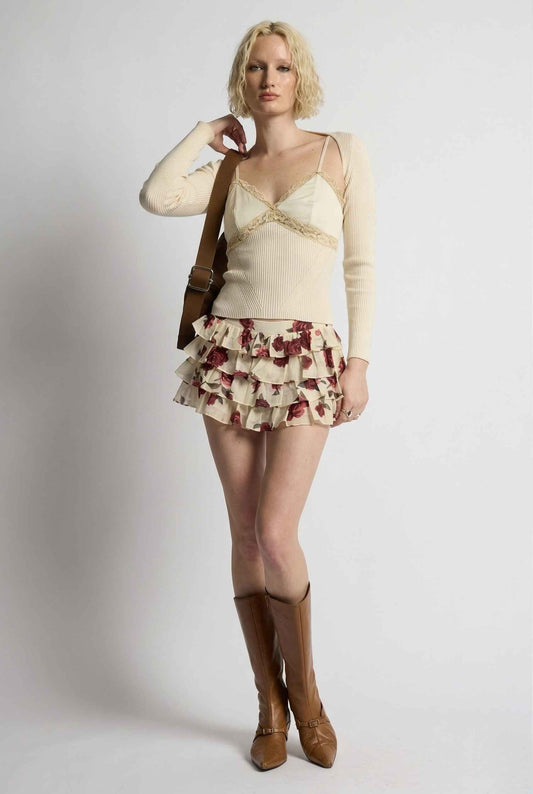 Woman wearing a cream top and Juliet Skort Cream & Burgundy Rose Floral Lyocell Ruffle Mini Skort with brown boots on a white background