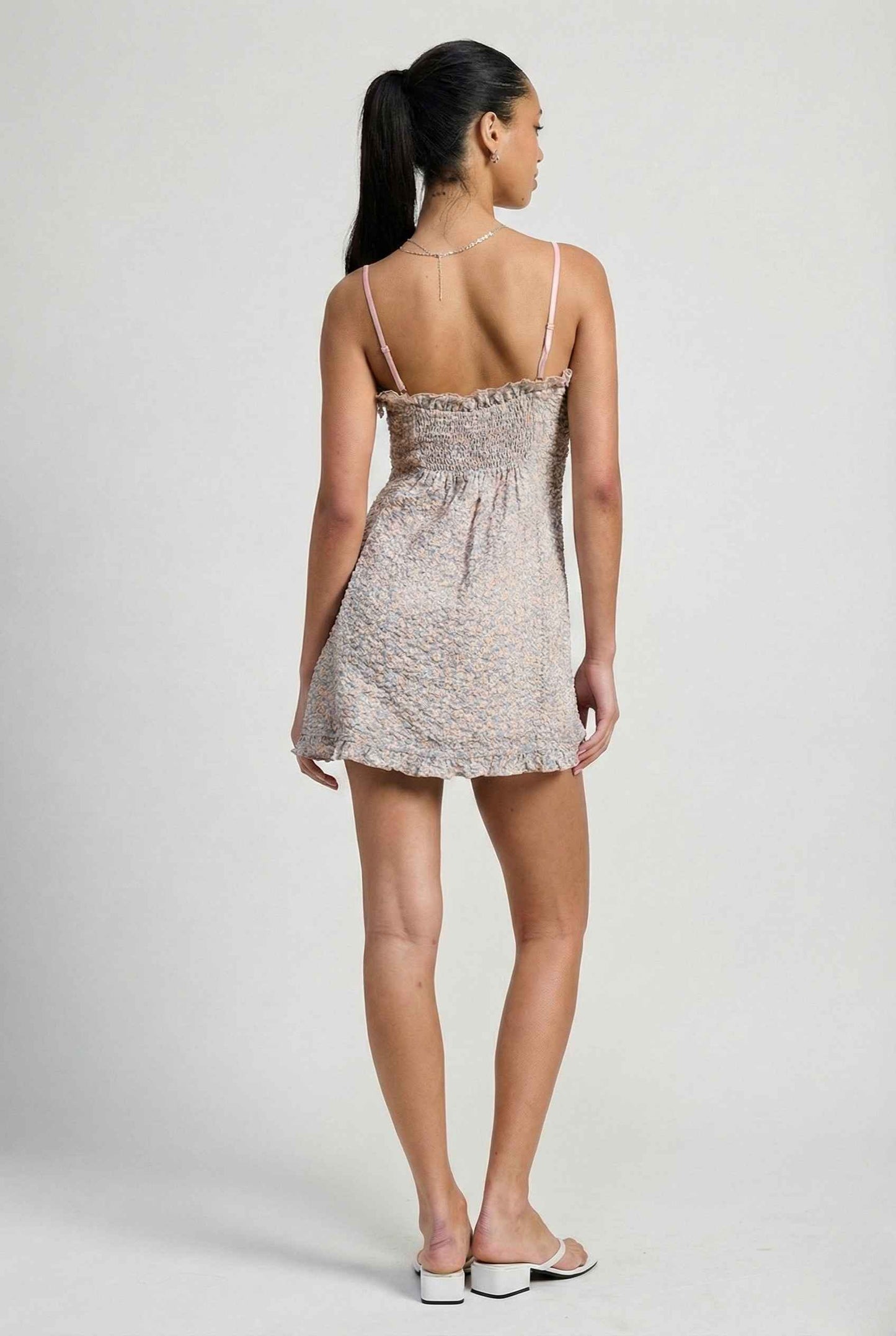 Woman wearing a Kaia Mini Pink Pastel Floral Ruffle Tie Dress on a plain background