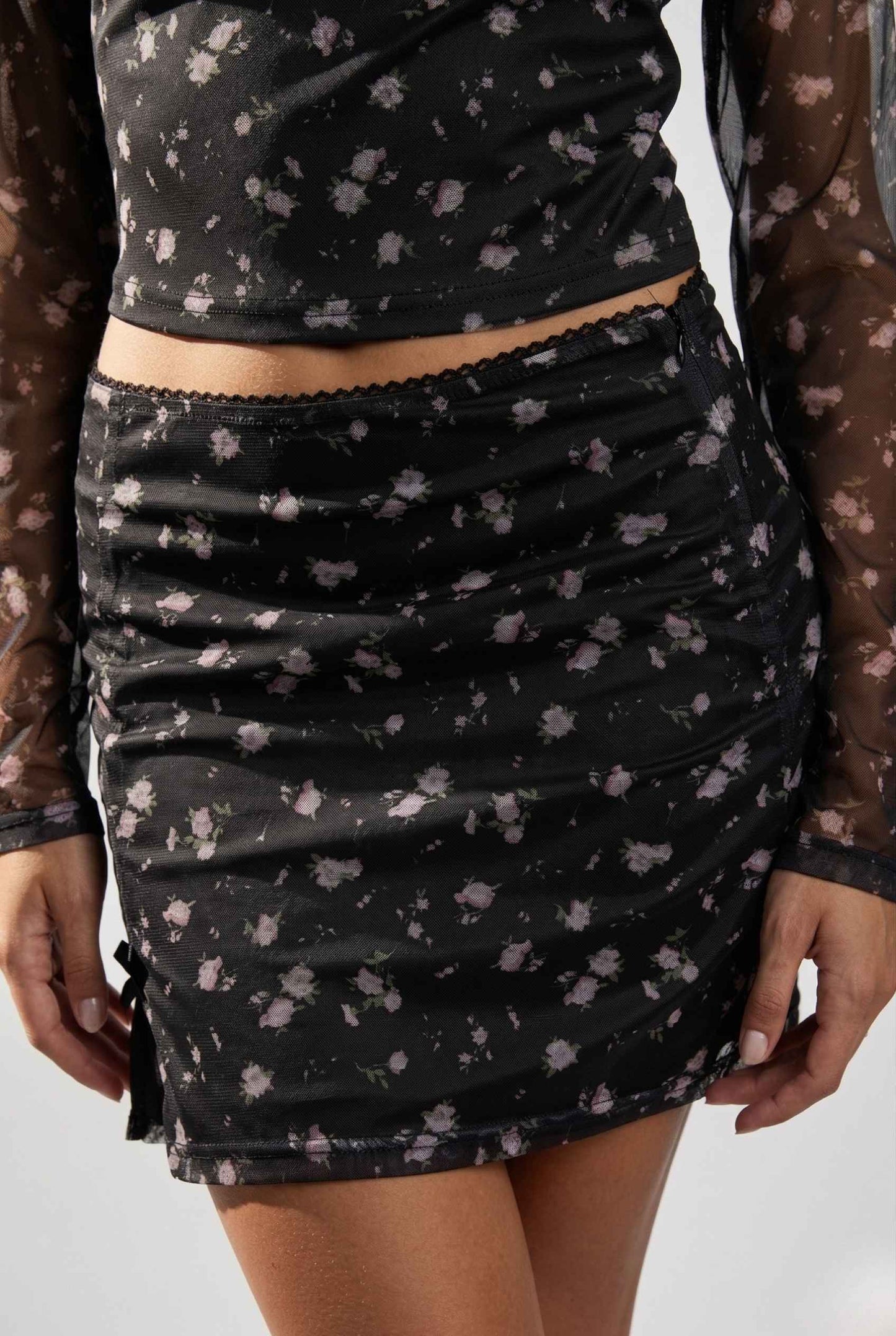Kaia Skirt Black Ditsy Floral Stretch Mesh Mini Skirt worn by a woman on a plain background