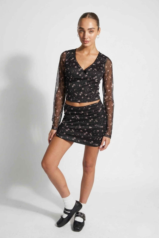 Woman wearing a black sheer top and Kaia Skirt Black Ditsy Floral Stretch Mesh Mini Skirt on a white background