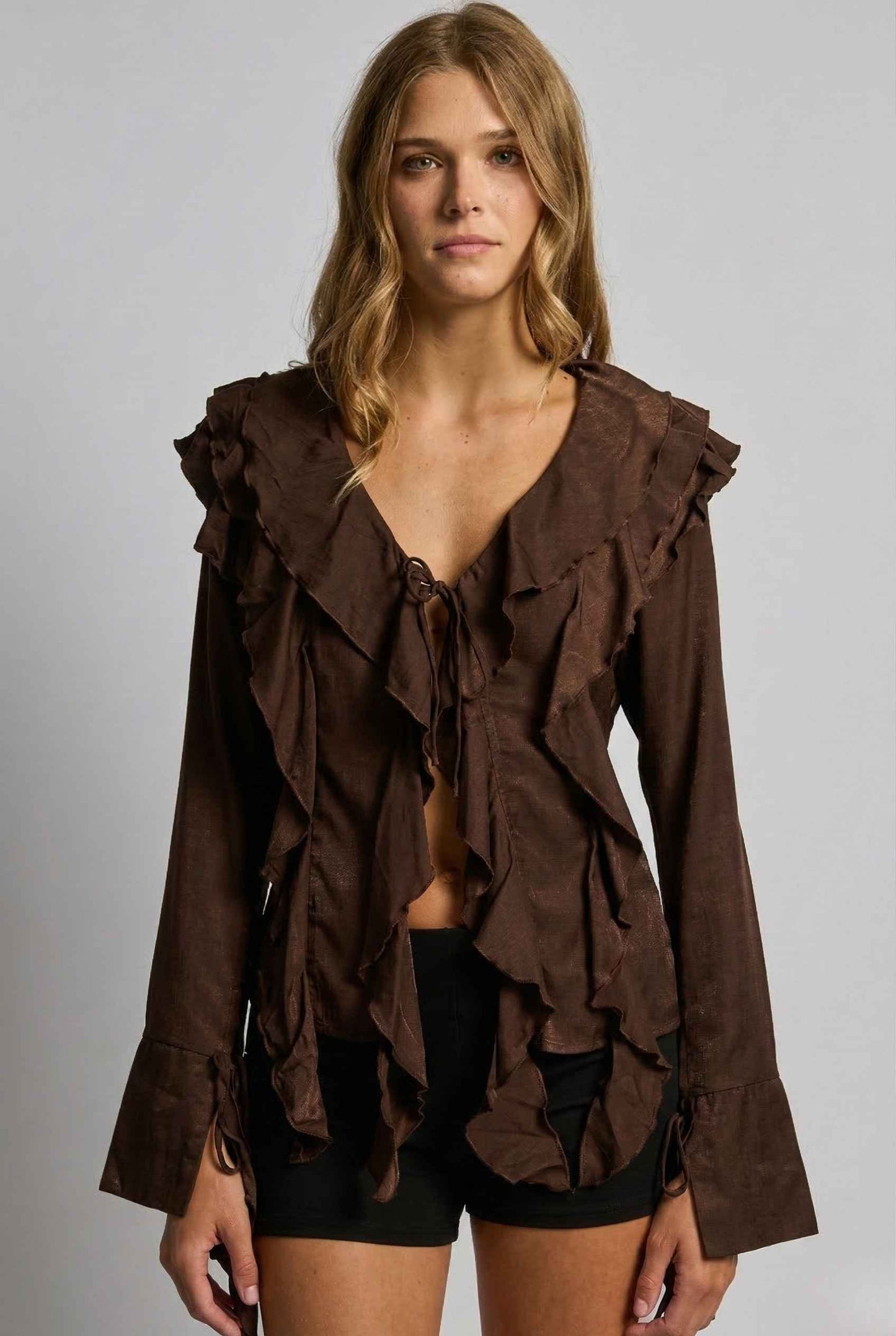 Woman wearing a Kaia Top Chocolate Brown Ruffle Tie-Front Long Sleeve Blouse against a gray background