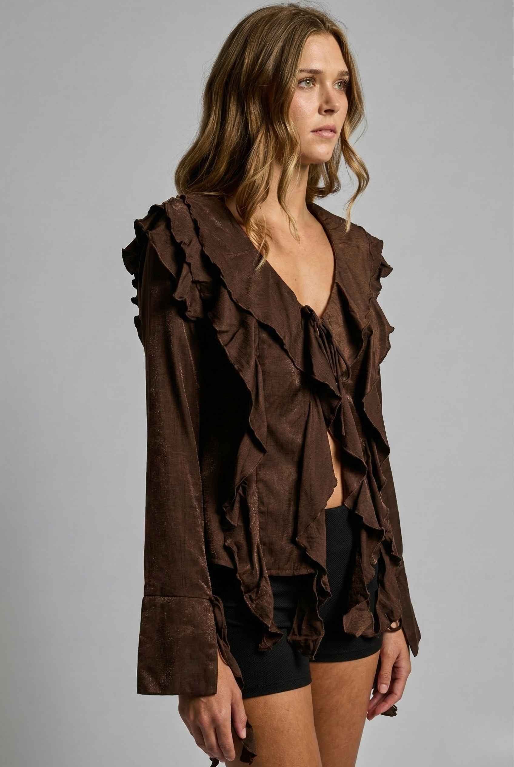 Woman wearing a Kaia Top Chocolate Brown Ruffle Tie-Front Long Sleeve Blouse against a gray background