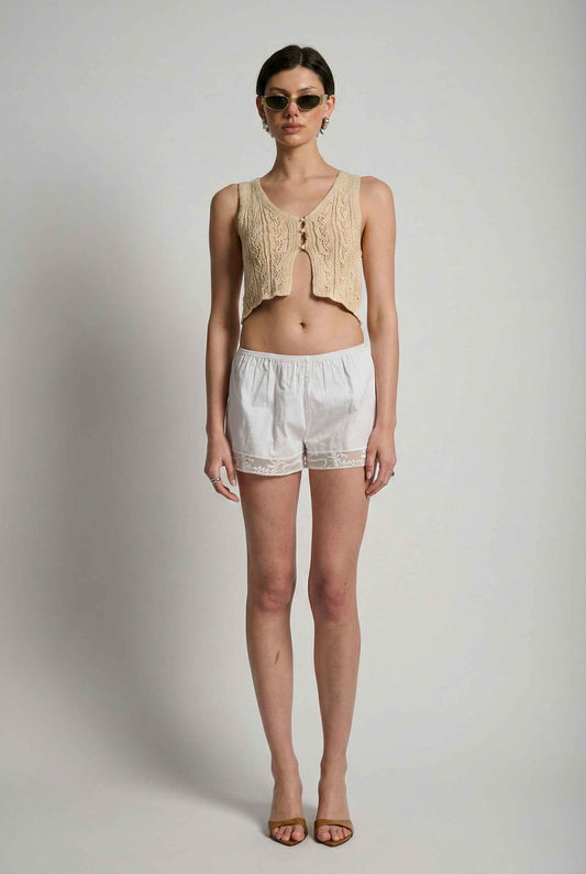 Model wearing Kaia Top in Cream Crochet Button-Front Split Hem Crop Vest with crochet shorts and open toe heels on a plain background