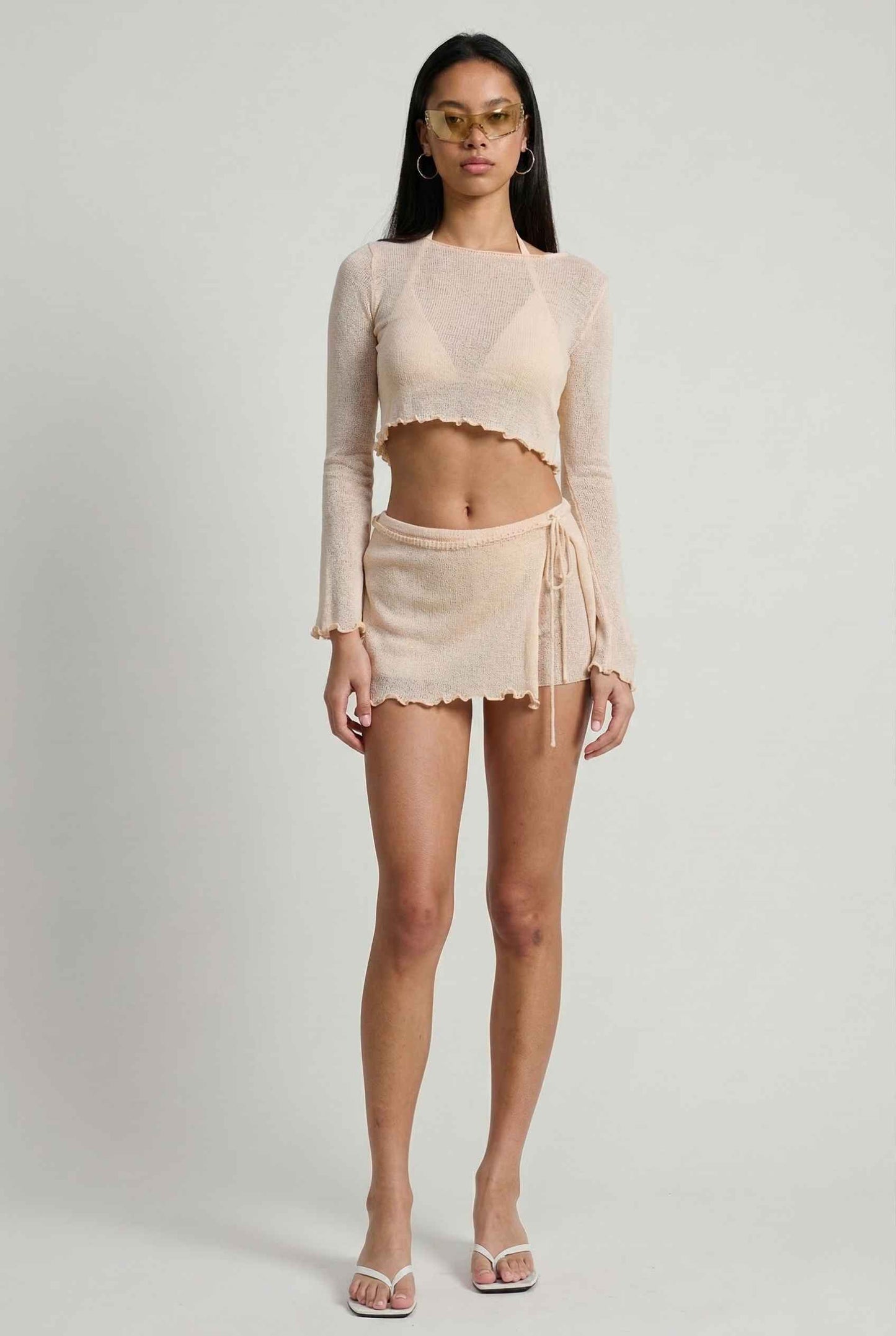 Woman wearing a Kaia Top Cream Sheer Knit Boat Neck Long Sleeve Crop and skirt set on a plain background