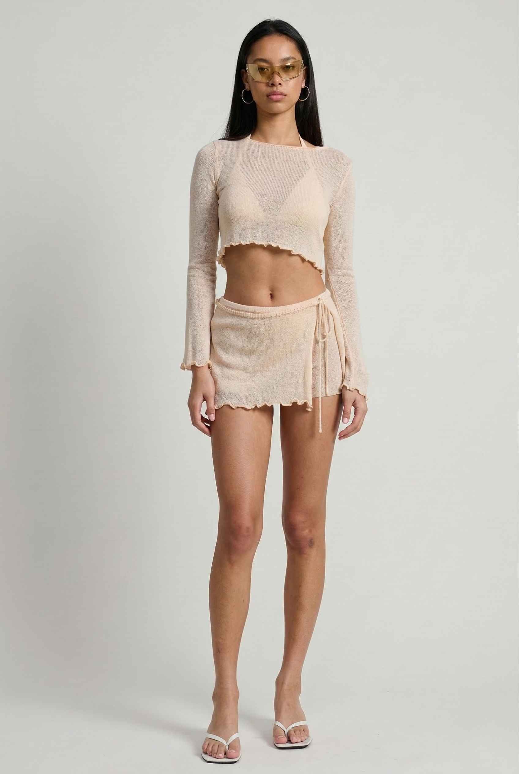 Woman wearing a Kaia Top Cream Sheer Knit Boat Neck Long Sleeve Crop and skirt set on a plain background