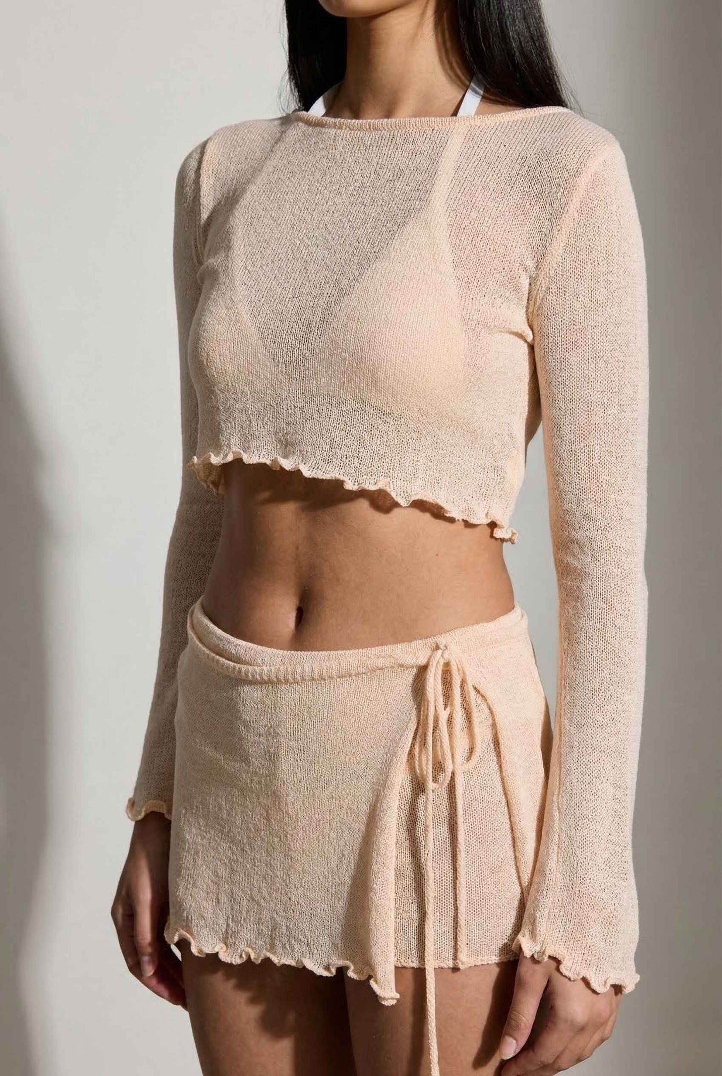 Woman wearing a sheer beige long-sleeve top and shorts against a plain background