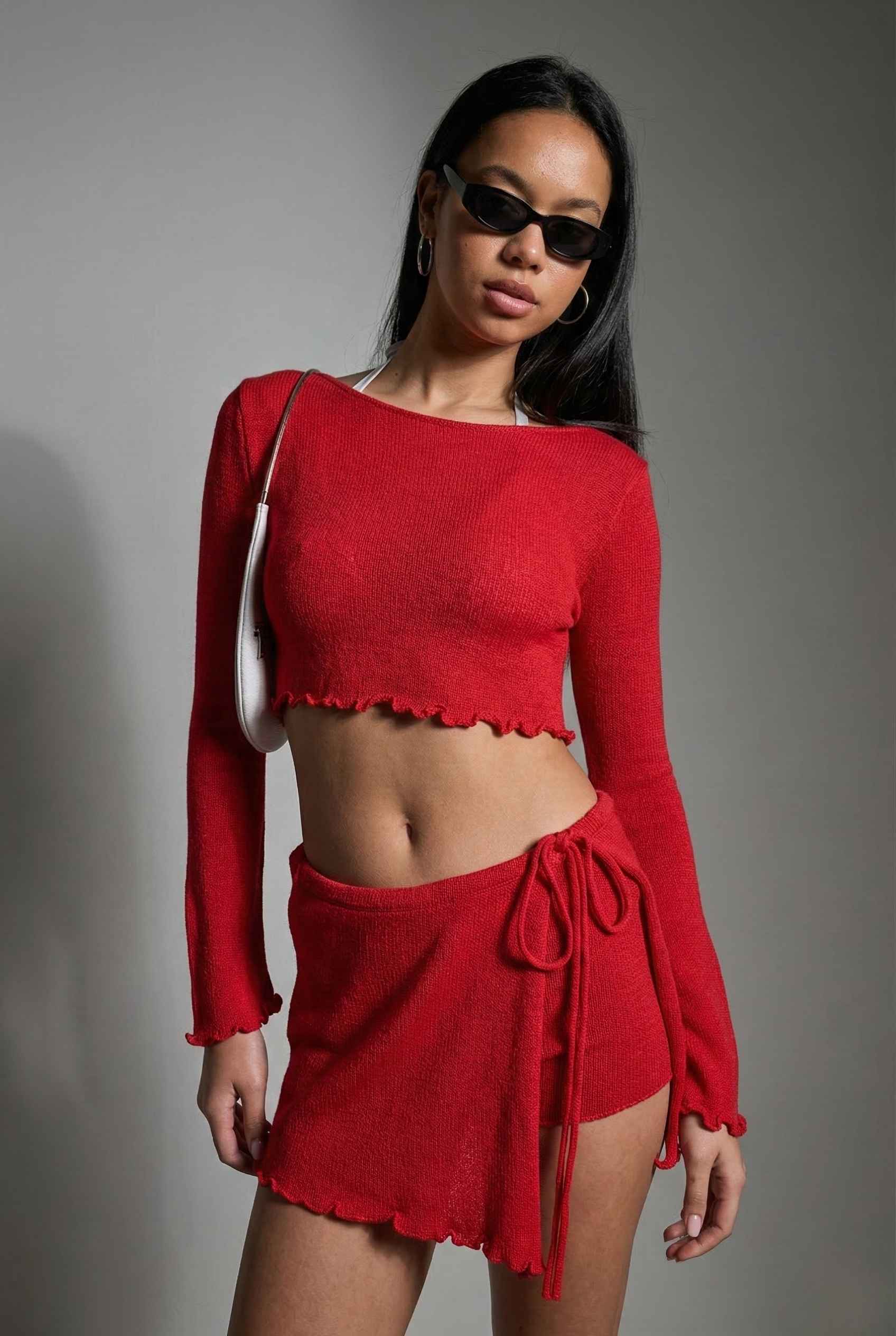 Woman wearing a Kaia Top Red Sheer Knit Boat Neck Long Sleeve Crop with a gray background