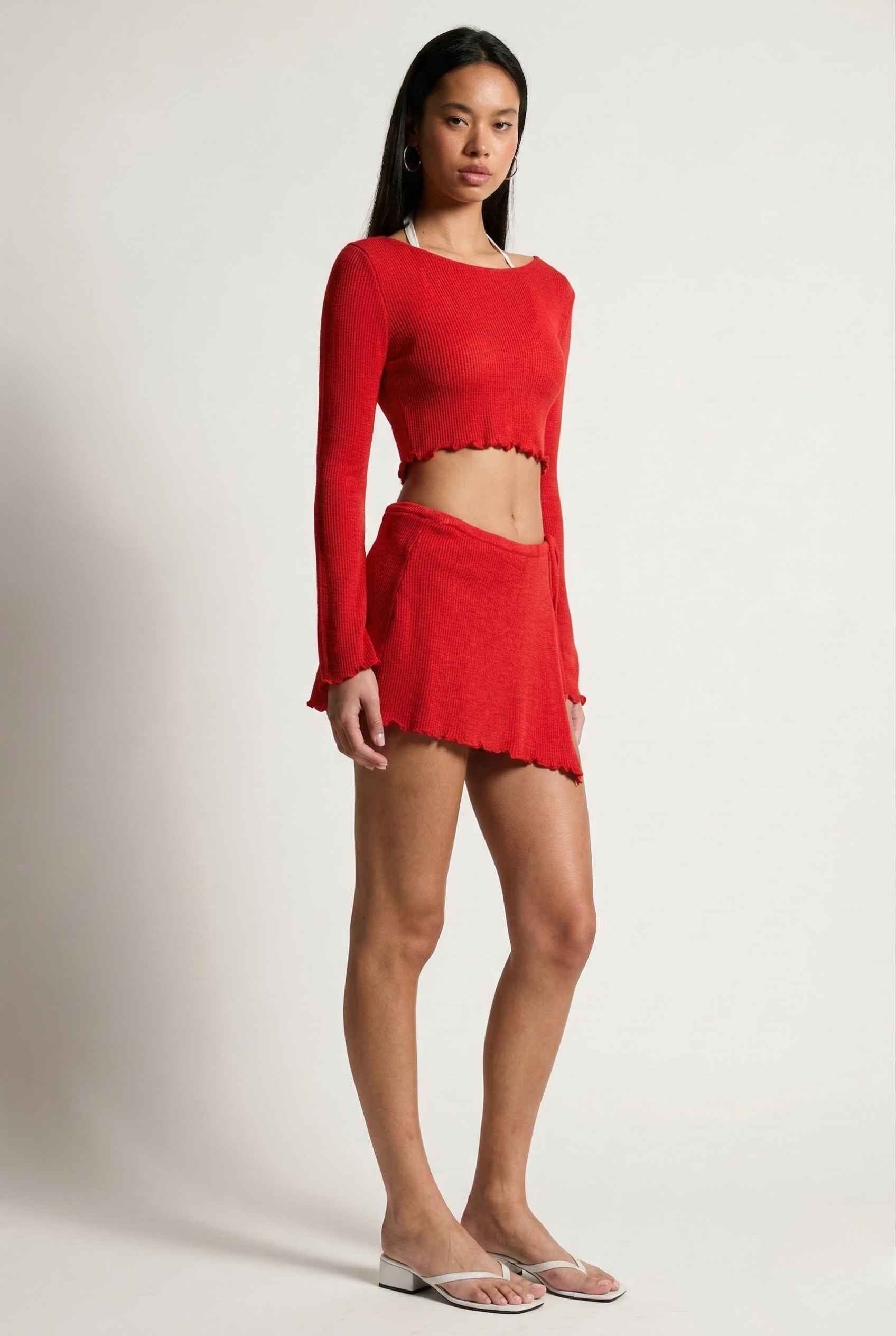 Woman wearing a Kaia Top Red Sheer Knit Boat Neck Long Sleeve Crop on a plain background