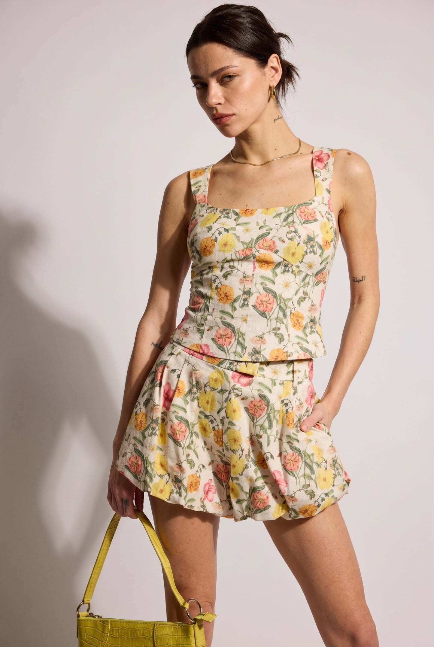Model wearing Kalani Floral High-Waisted Pleated Cotton Shorts in Yellow paired with matching tank top and handbag